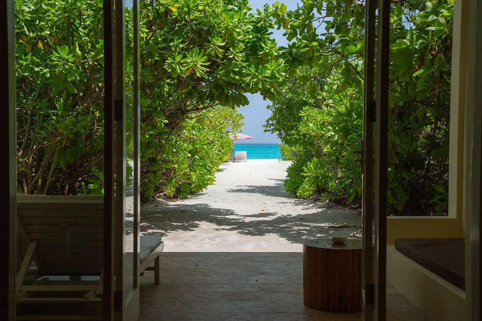 Dalla porta di un Deluxe Beach Bungalow un corridoio di sabbia fra gli arbusti porta dritto al mare.