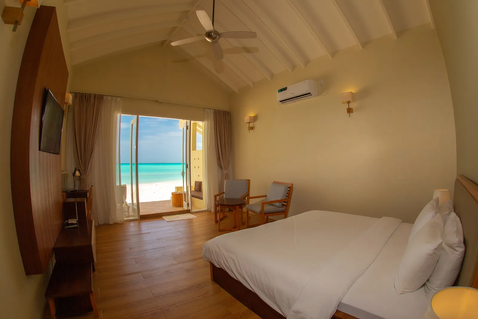 La camera di un Superior Beach Bungalow: il letto, il parquet, il ventilatore al soffitto e la porta aperta sulla spiaggia e sul mare.