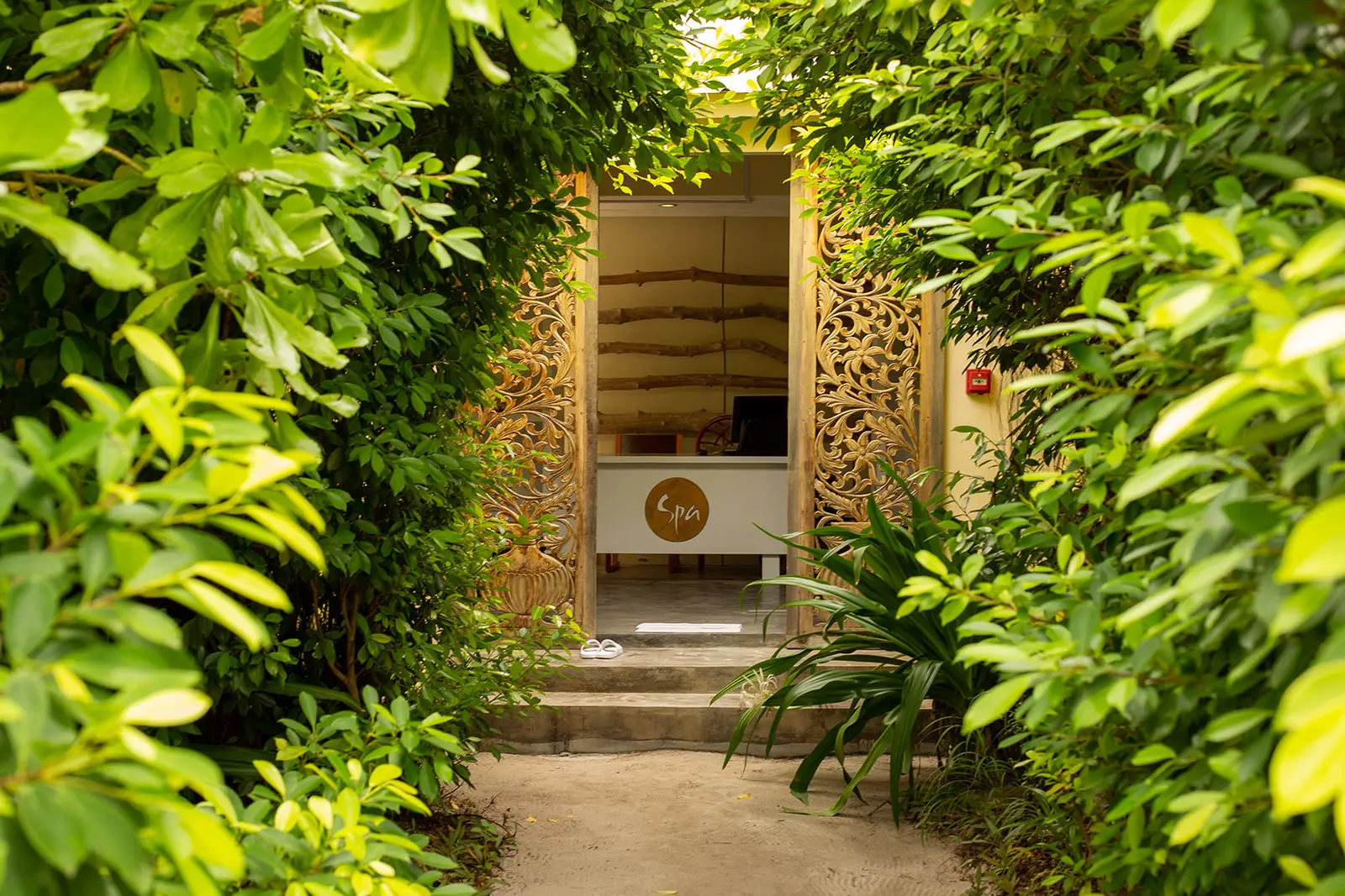 L’ingresso della spa in fondo a un sentiero fra la vegetazione fitta, con le porte di legno intagliato.