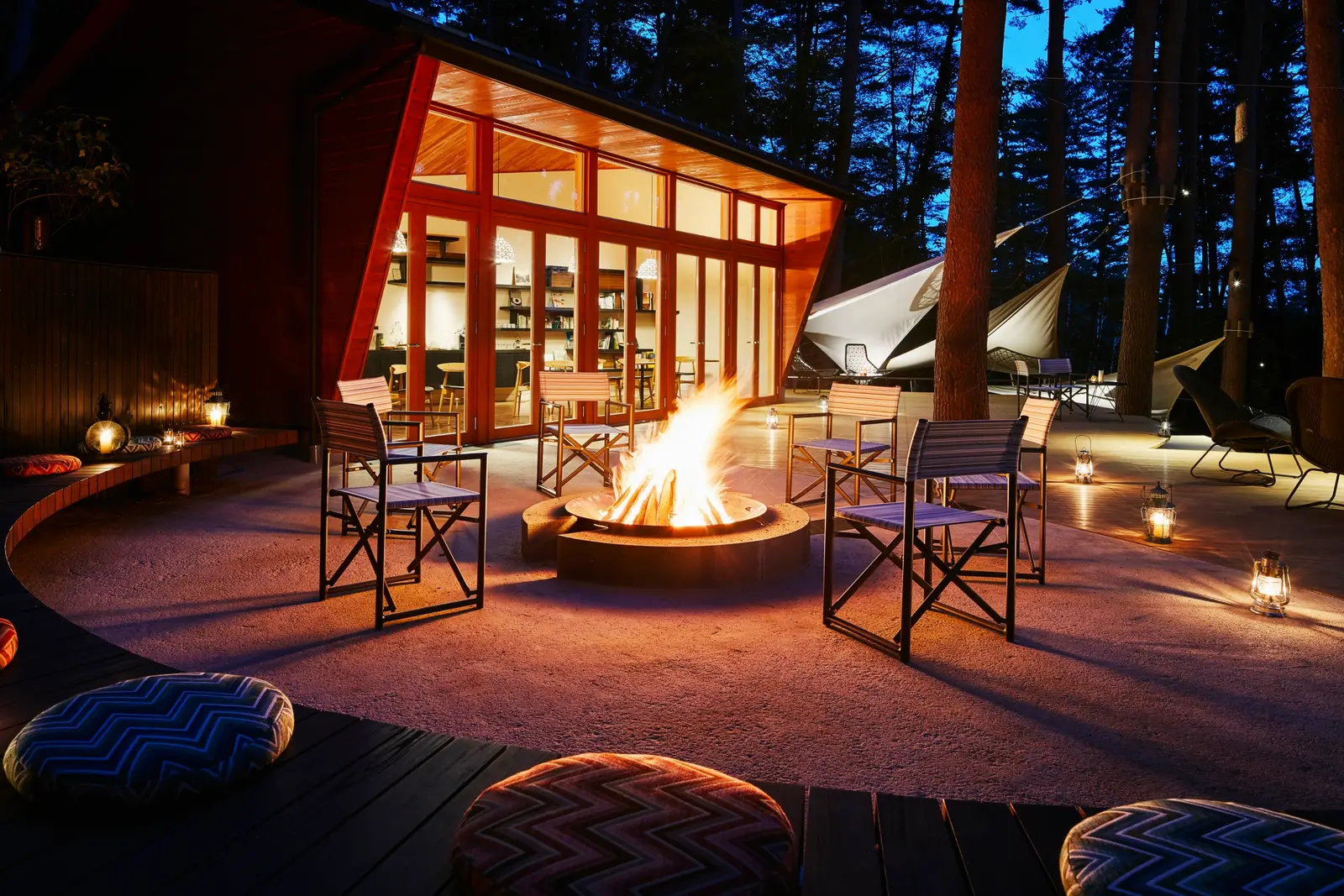 A fire pit on the Cloud Terrace at night, chairs around it and the Library Cafe lit behind