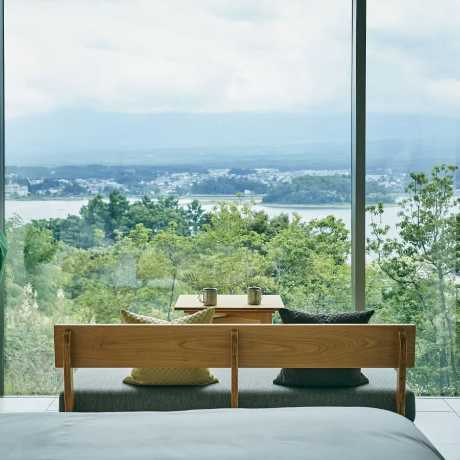 A king bed facing a full-height window, a terrace bench and the lake beyond