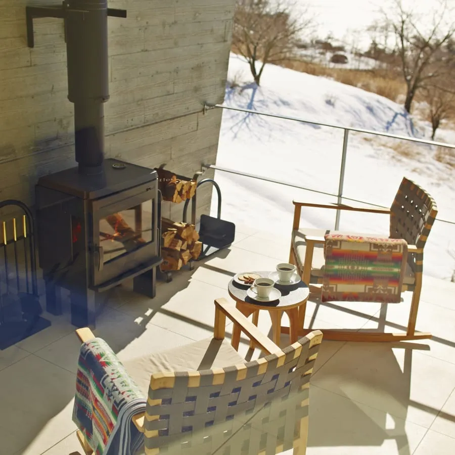A cabin terrace in winter: a wood stove, 2 chairs and snow on the slope