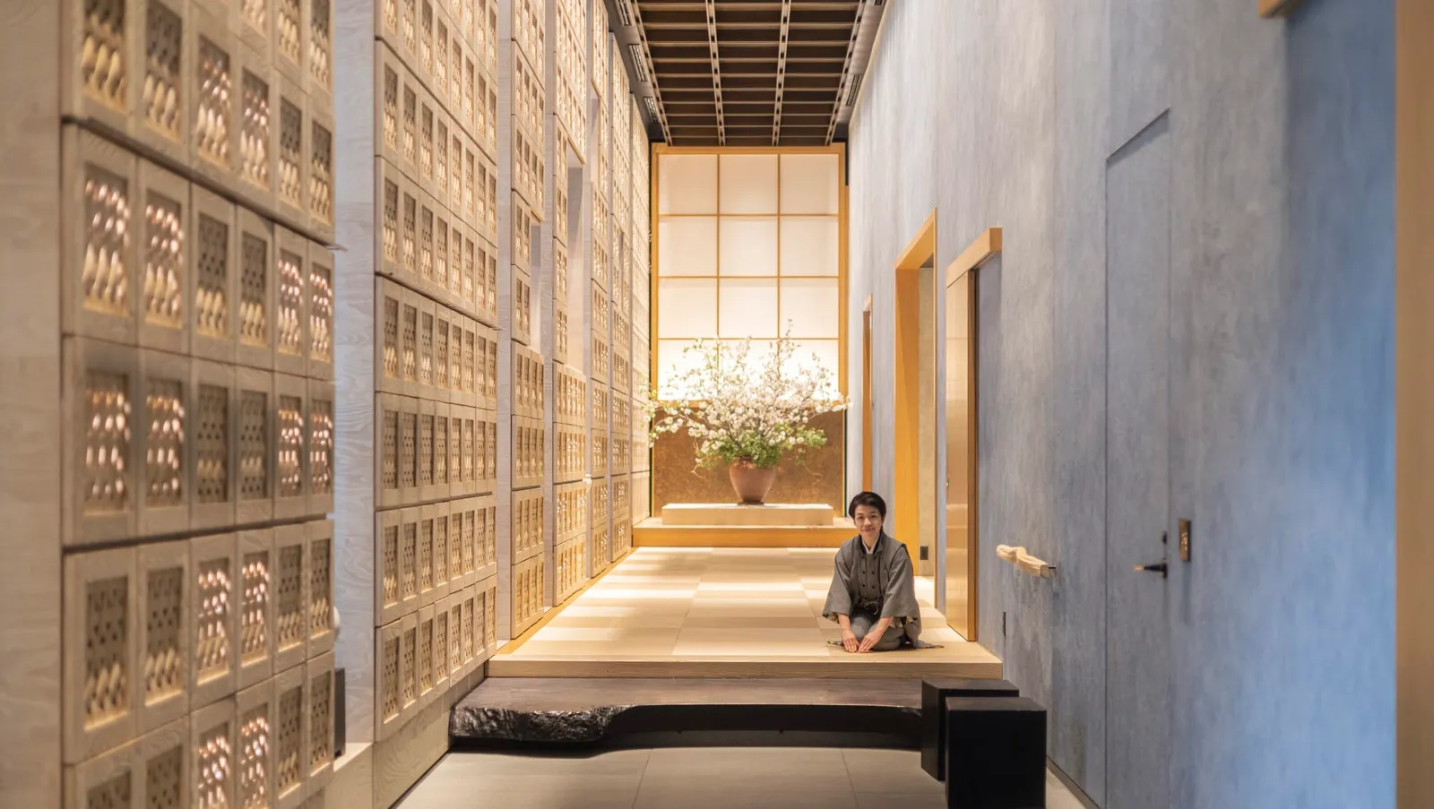 The tatami-floored entrance, its wall of pierced-wood shoe lockers and a guest sitting in a kimono.