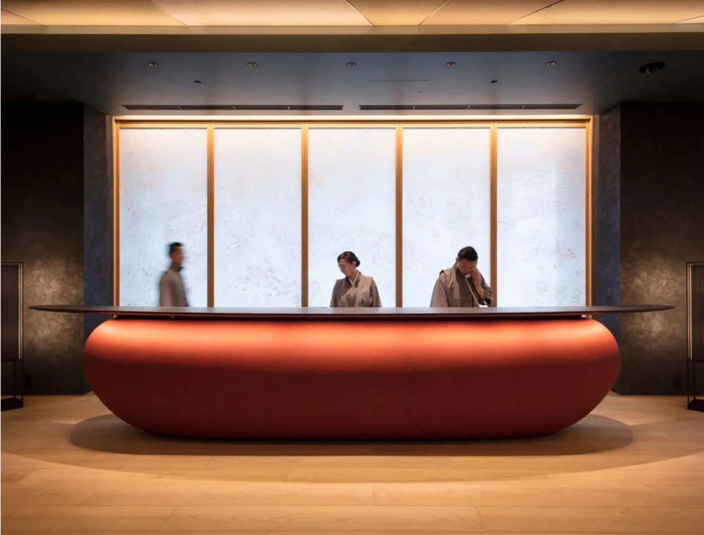 The reception counter, red and curved, before a tall rice-paper window, with 3 staff.