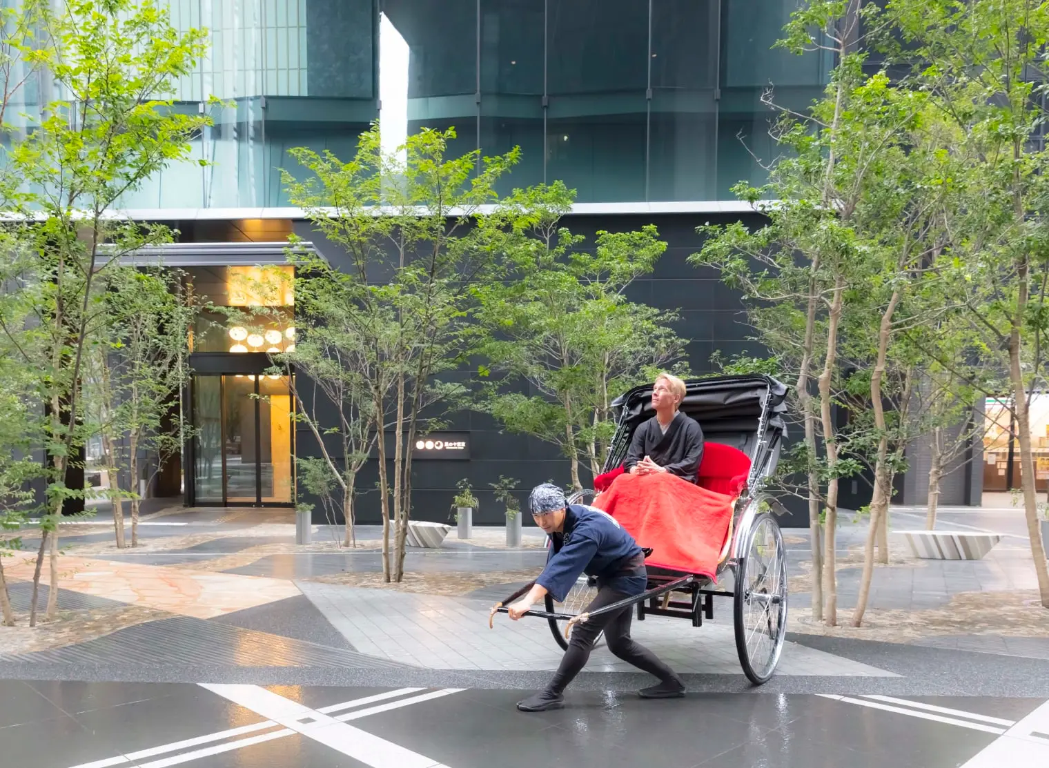 A red rickshaw sets off from the hotel garden among the trees, the Otemachi towers behind.