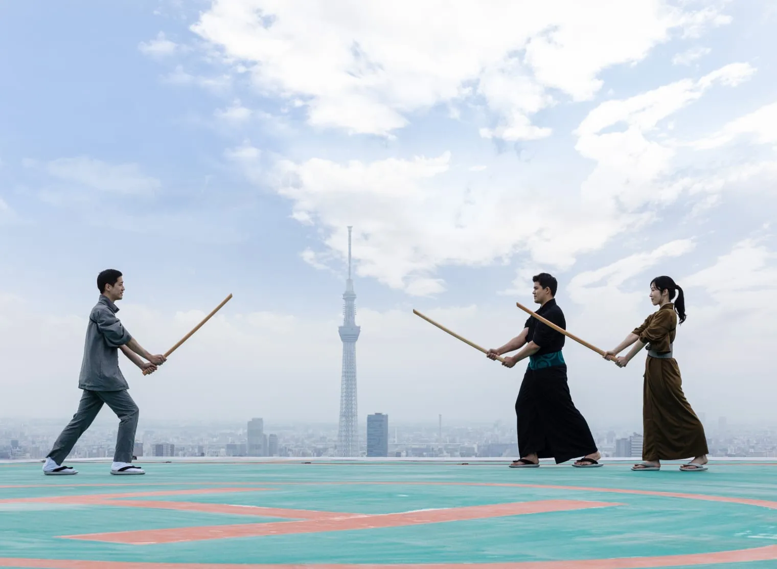 3 people with wooden swords on a rooftop above Tokyo, the Skytree on the horizon.