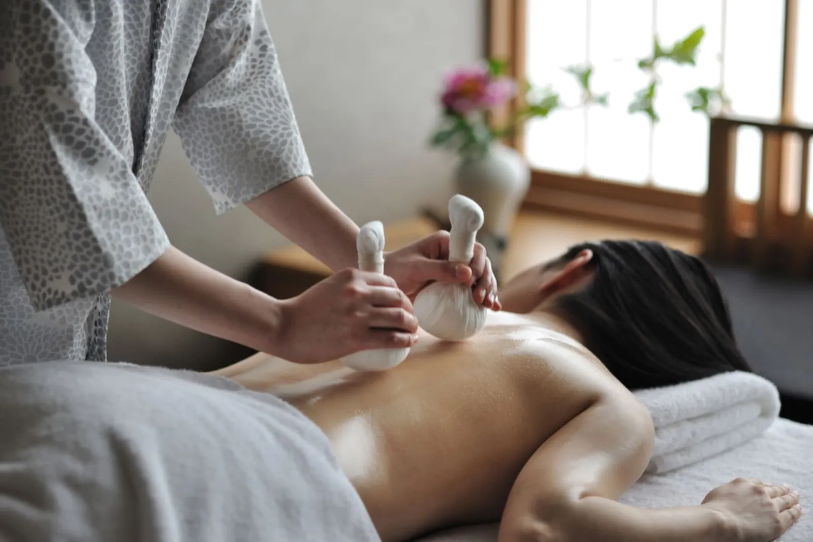 A spa treatment: the therapist presses warm herbal pouches on a guest’s back.