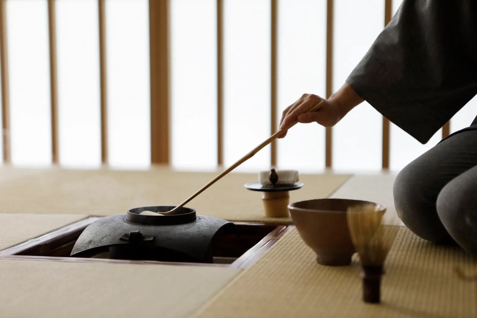 The tea ceremony: a hand pours hot water with the bamboo ladle beside the bowl and the whisk.