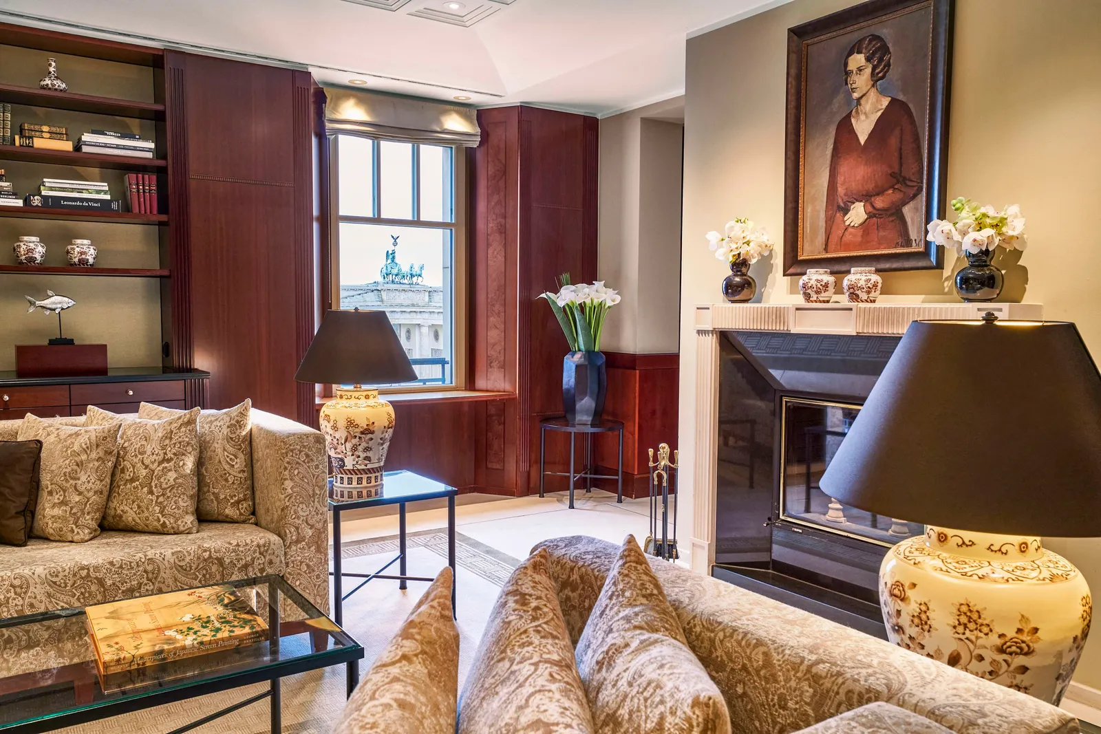 Adlon Deluxe Suite with armchairs, a portrait above the fireplace and a doorway to the bedroom.