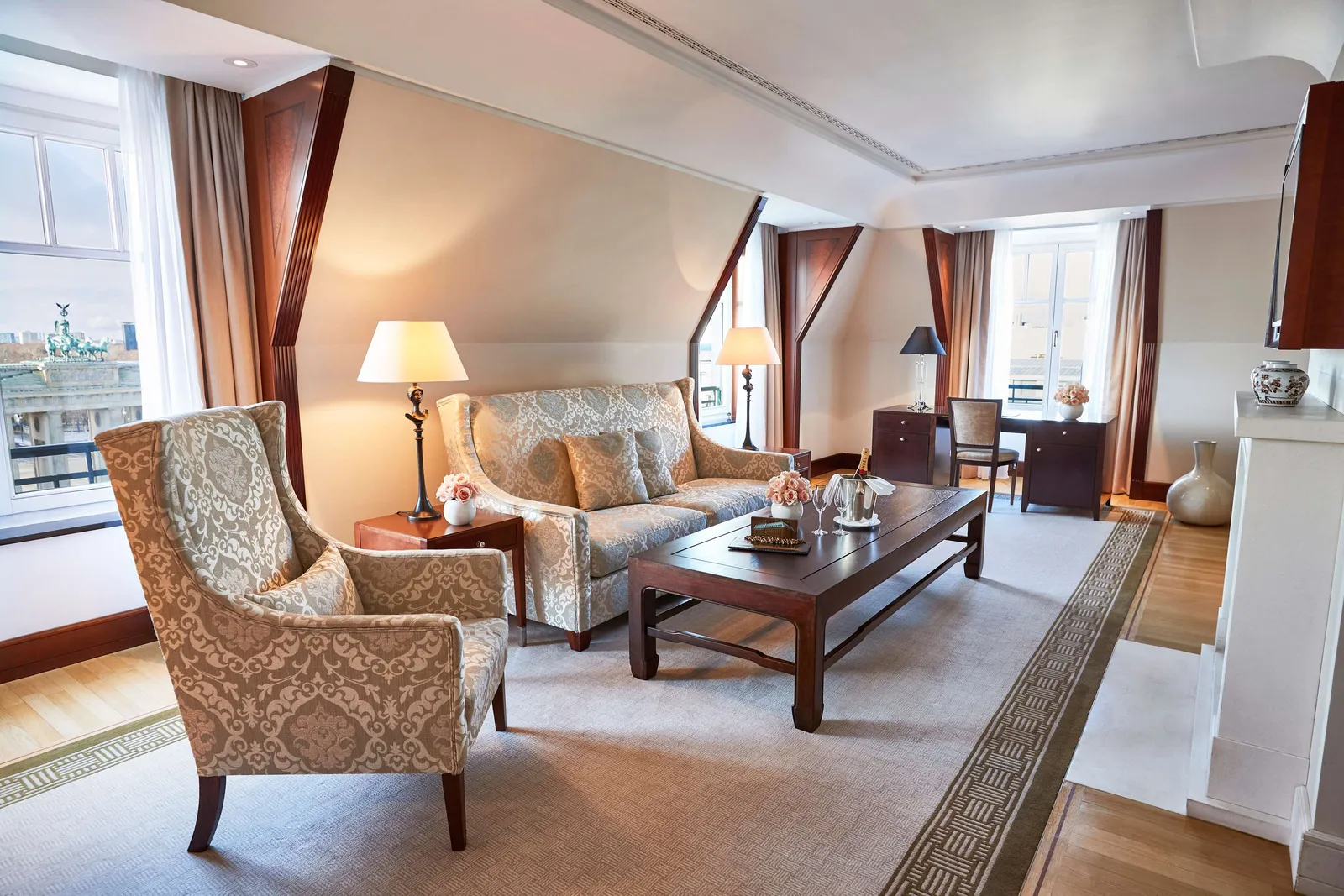 The Brandenburg Gate Deluxe Suite living room with floral armchairs, a sofa and windows along the wall.