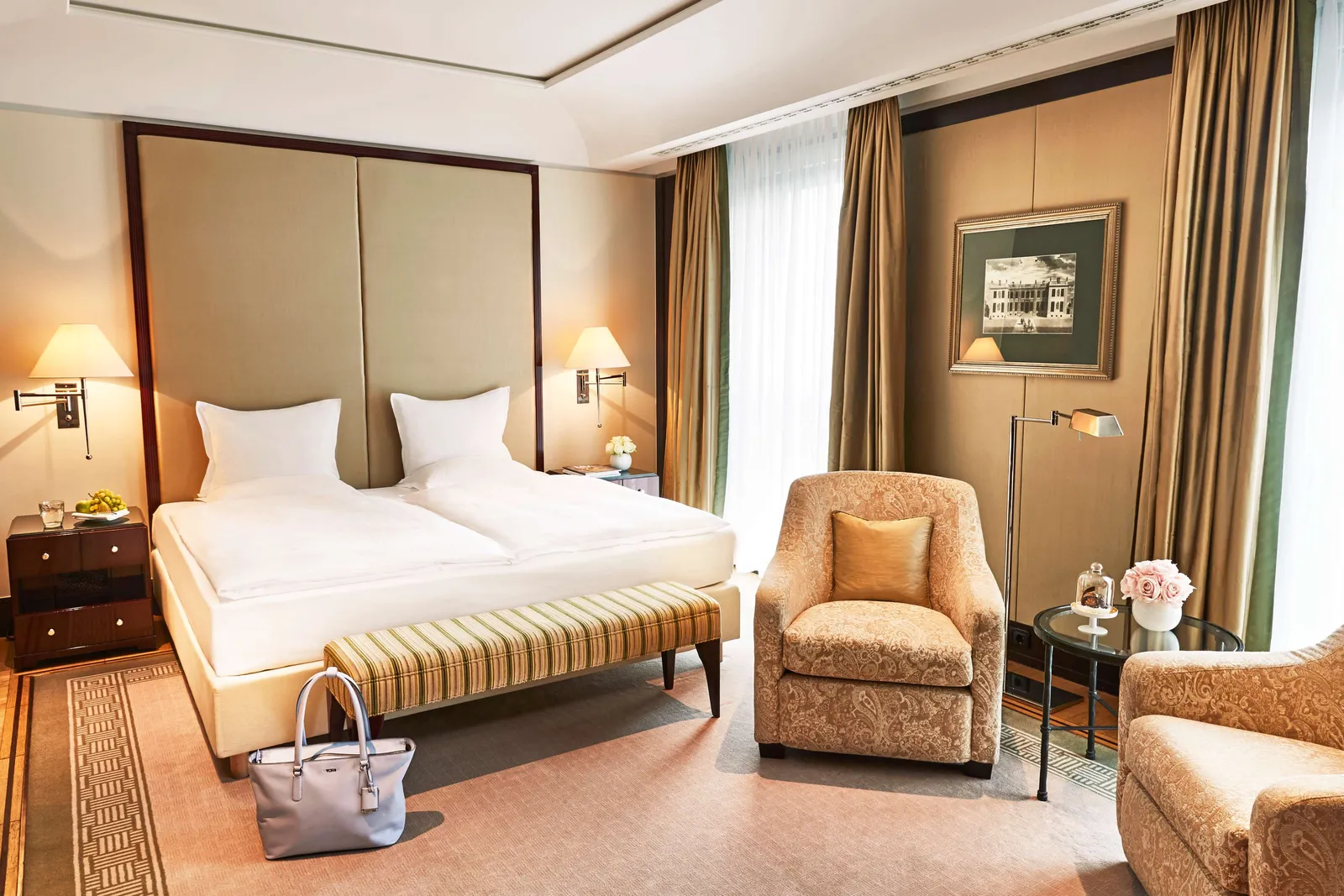 Executive Room with a double bed, striped bench and pale armchairs beside the window.