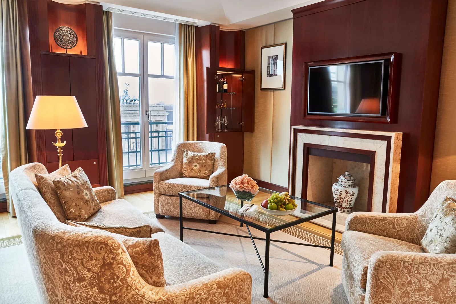 The Pariser Platz Suite living room, with floral armchairs, television above the fireplace and the Gate outside.