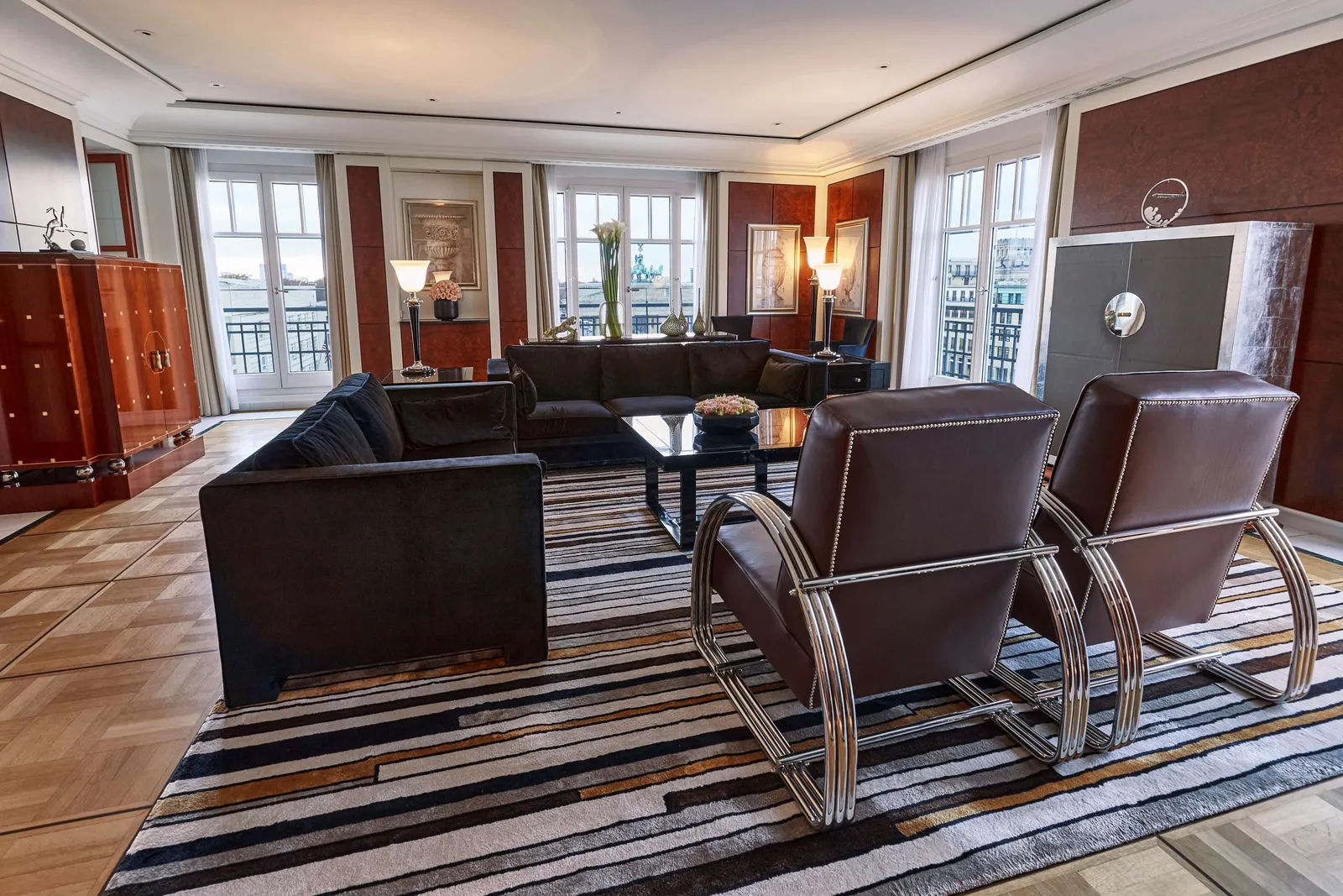 The Presidential Suite with dark living-room chairs and a dining area beside the windows.
