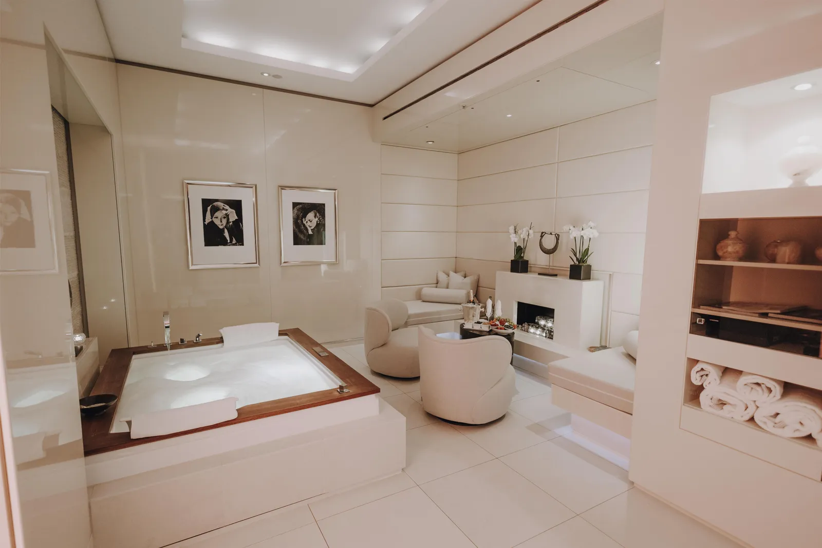 A private spa suite with a sunken whirlpool, pale chairs and 2 framed portraits.