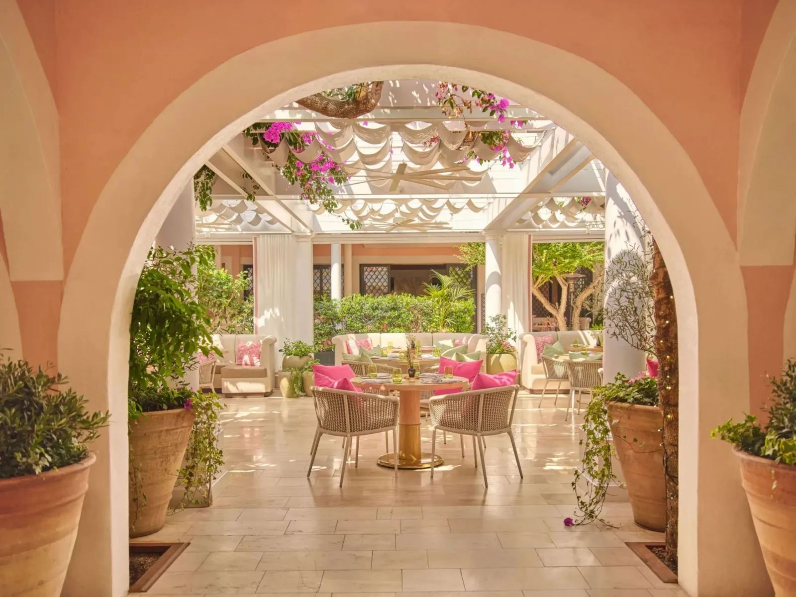 The pink arch leading into the restaurant, tables and fuchsia cushions under the pergola