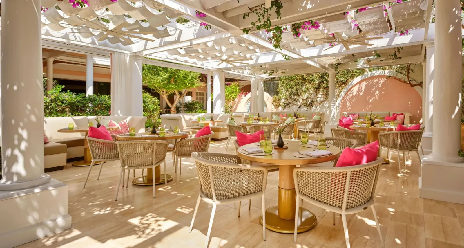 The restaurant terrace under the white pergola, with woven chairs and fuchsia cushions