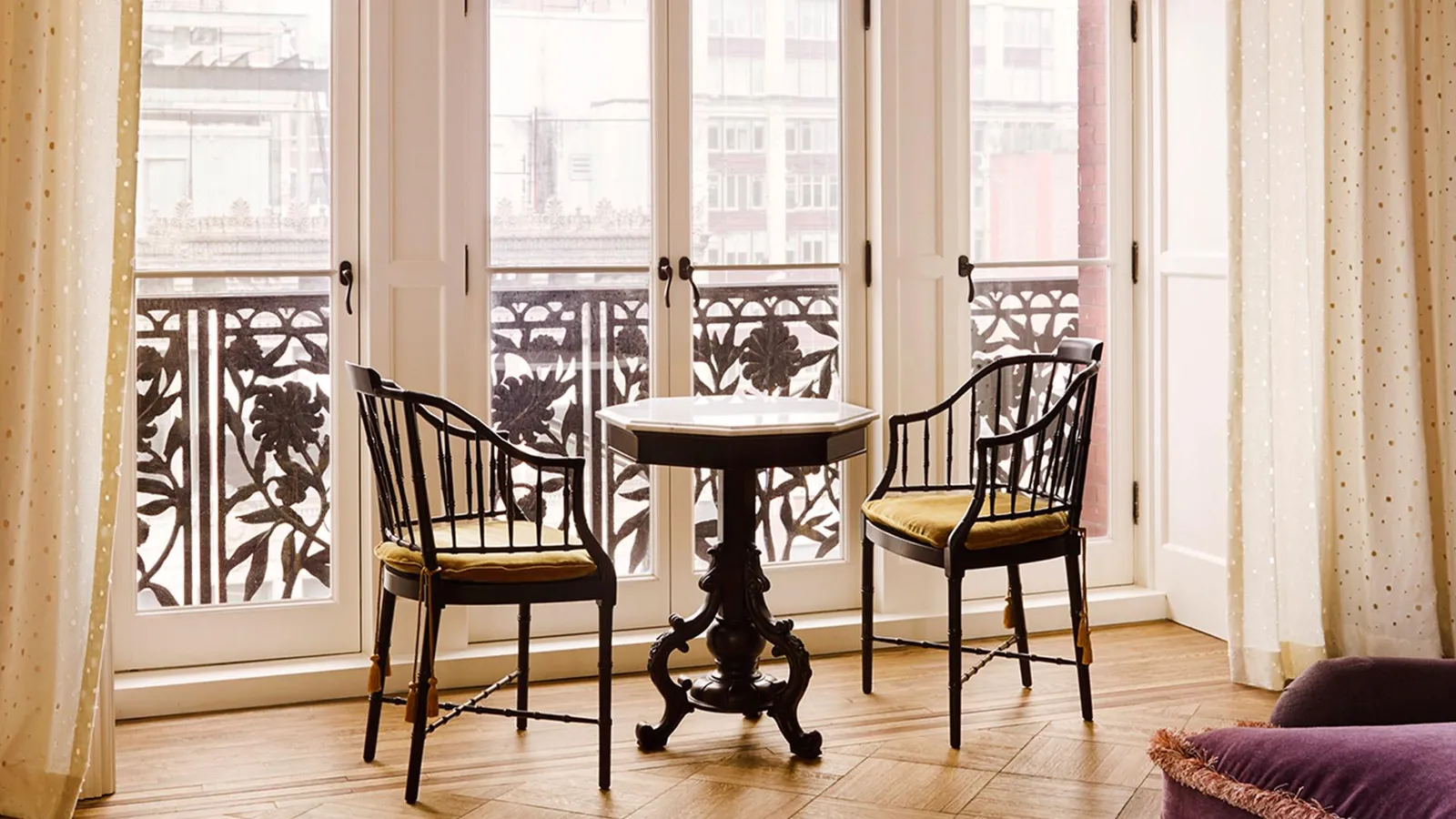 A small table and 2 chairs before the doors open onto the balcony