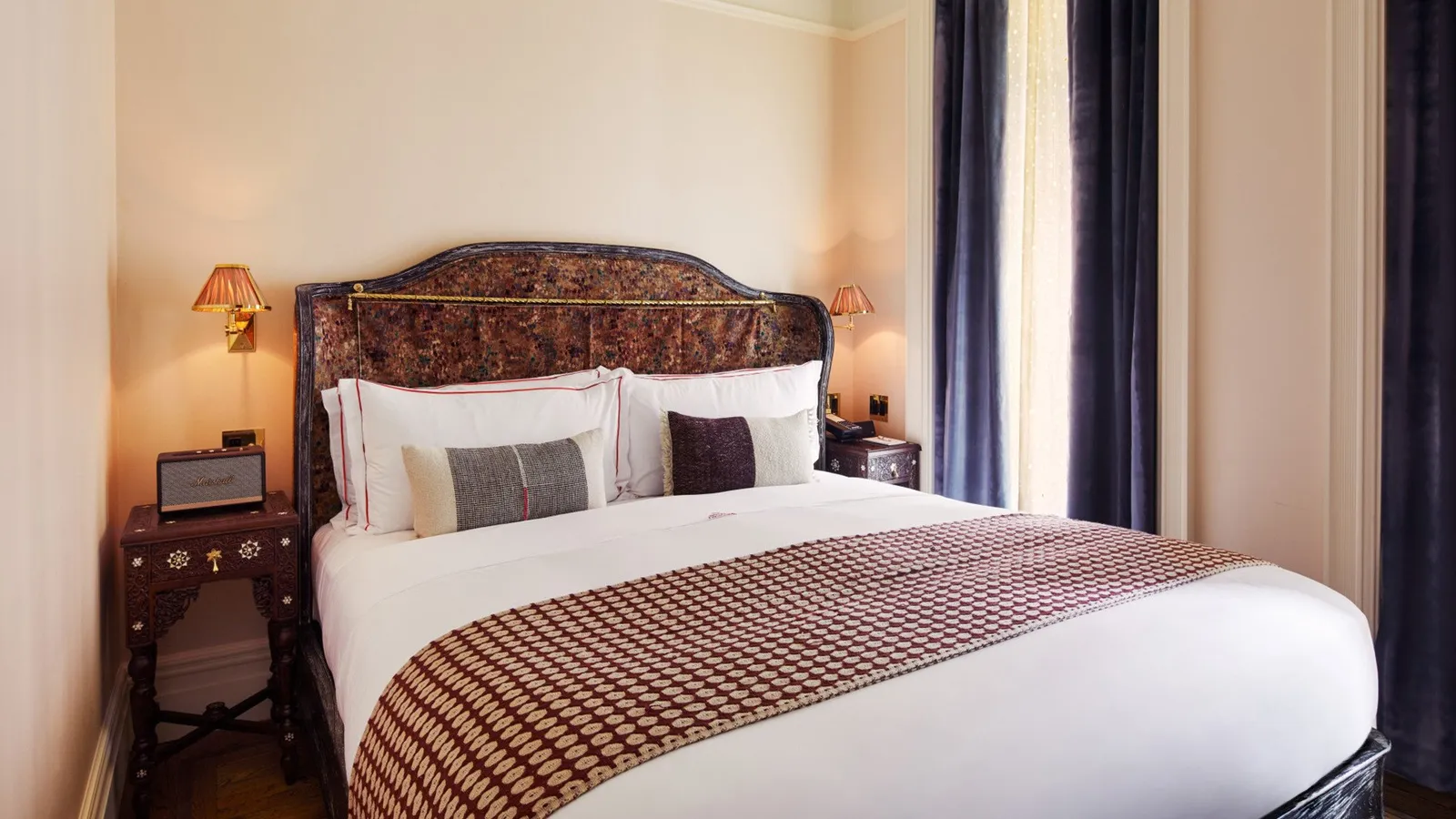 A Petite Chelsea: the bed with its carved headboard between 2 night tables and blue curtains