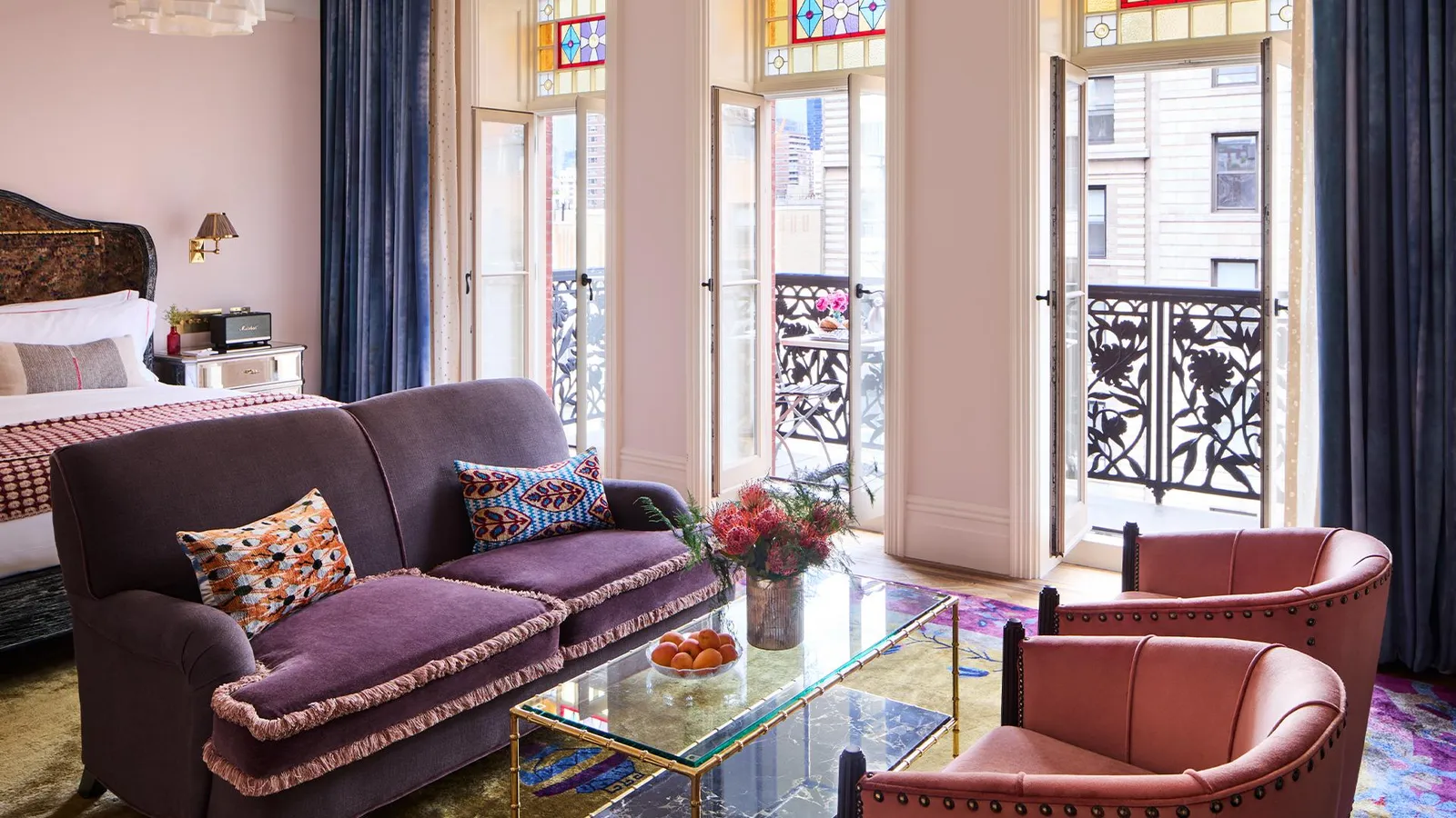 A living room with a purple sofa and pink armchairs, the doors open onto the iron balcony