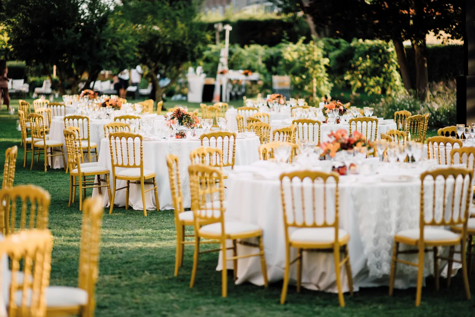 Round tables with white cloths and gilt chairs laid on the lawn of the Casanova Gardens.