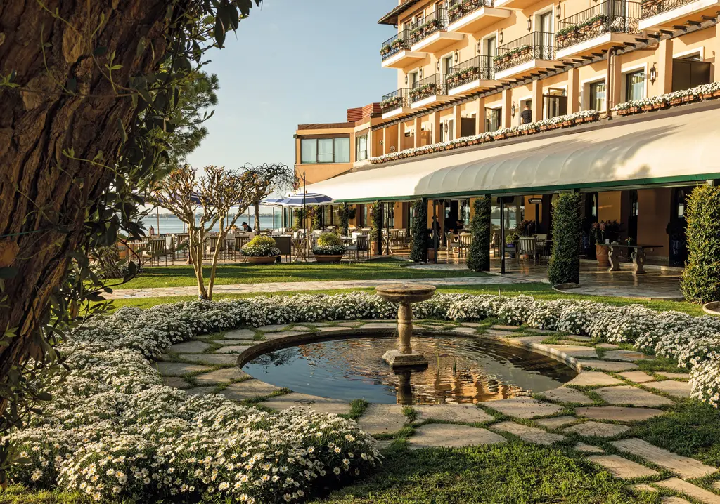 The garden with its stone basin among white flowers, before the balconied façade and the restaurant’s veranda.