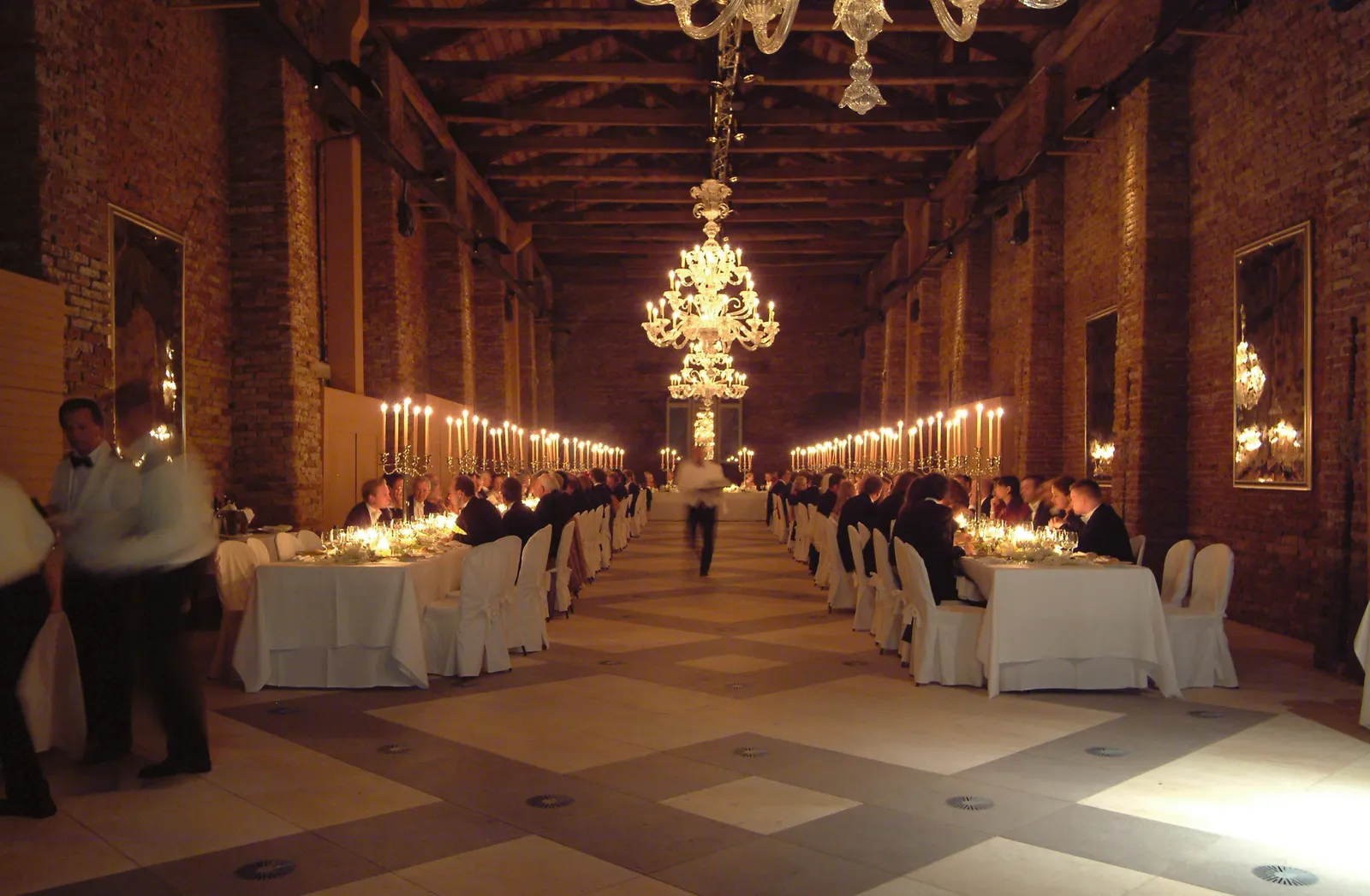 A dinner in the Granaries of the Republic: 2 long candlelit tables under the beams and a Murano chandelier.