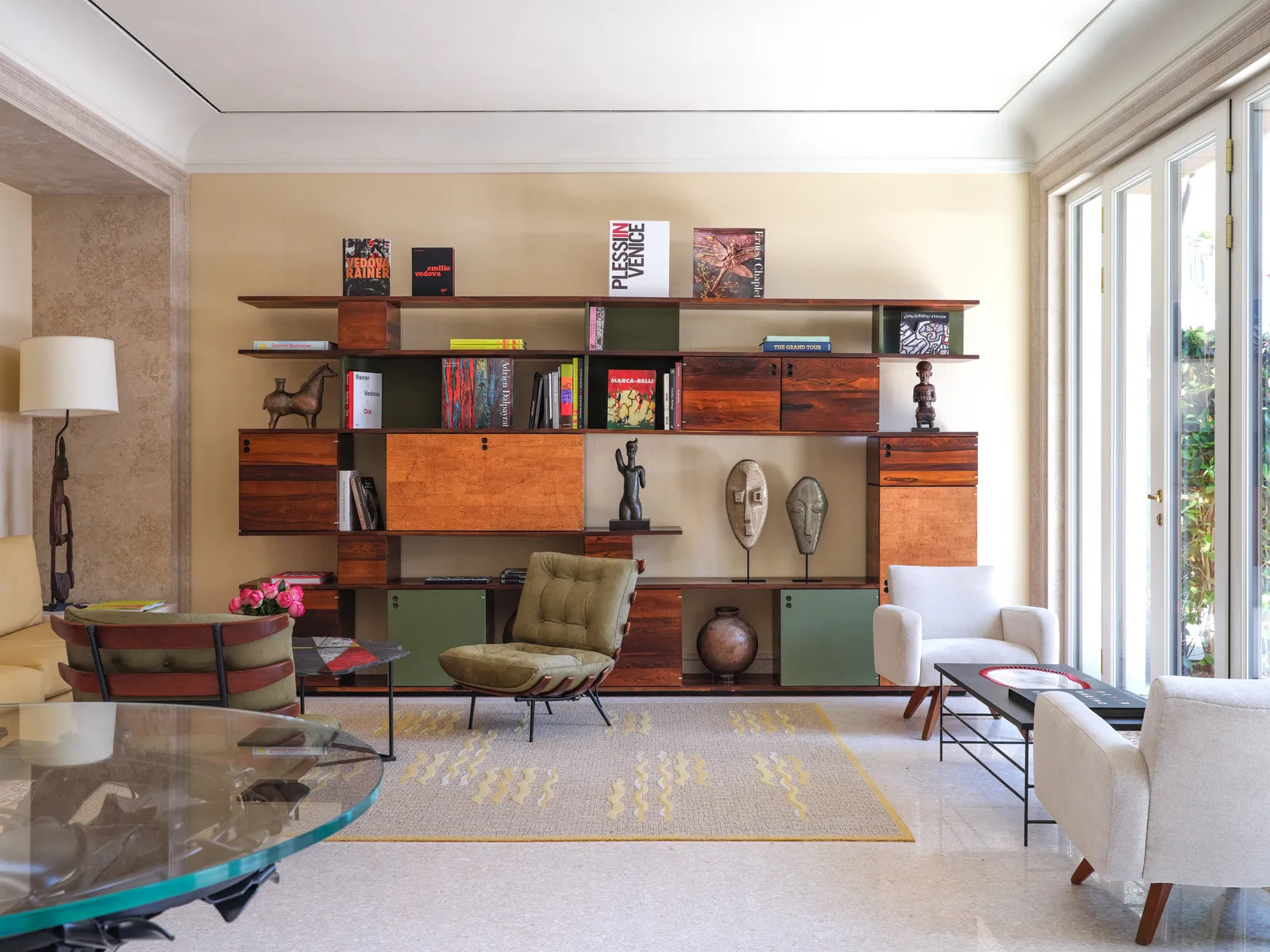 The library: a timber and brass bookcase with books and sculptures, pale armchairs and windows onto the garden.