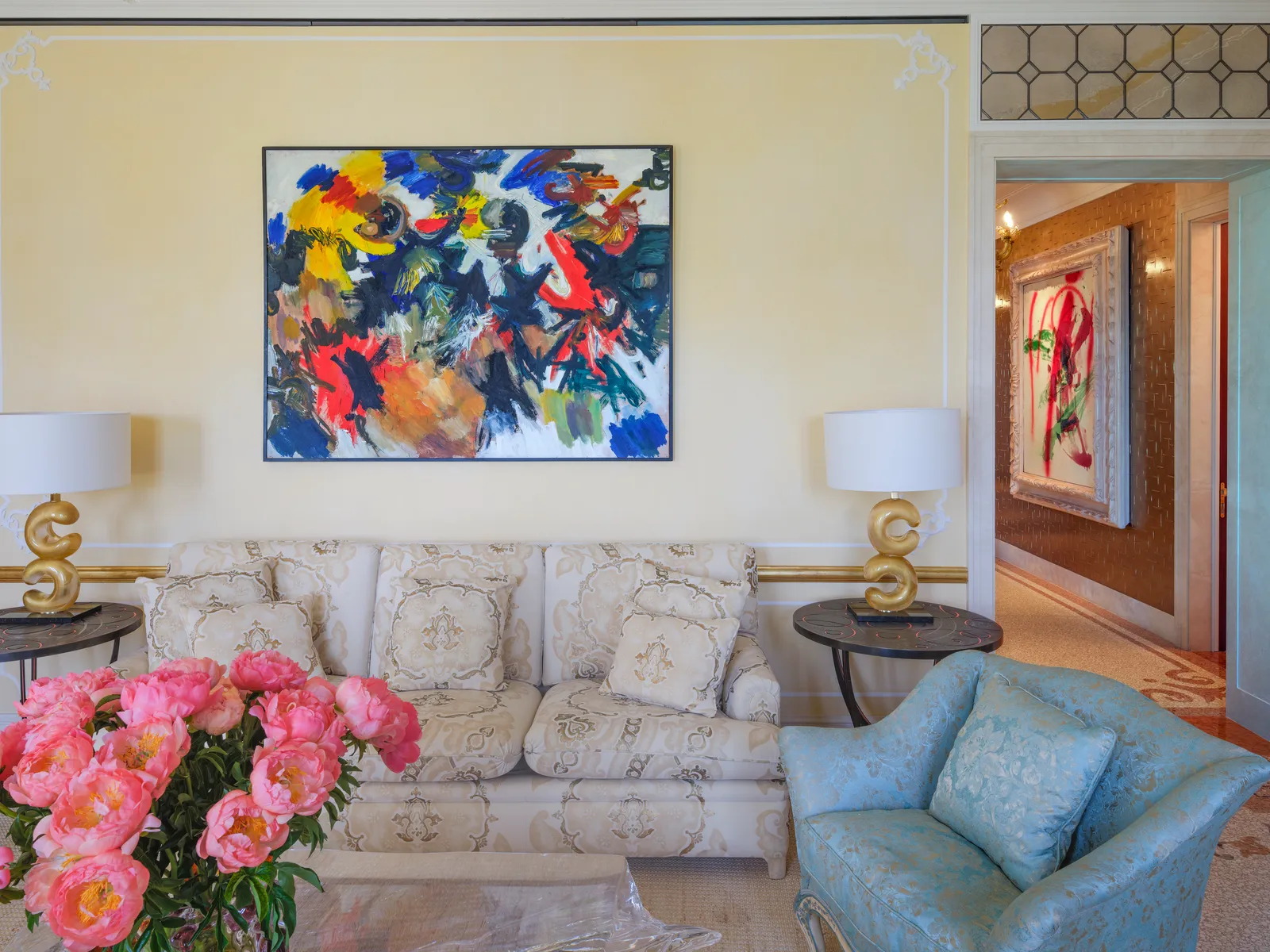 The Laguna Suite’s living room with a large colourful abstract painting, a pale sofa and pink peonies in front.
