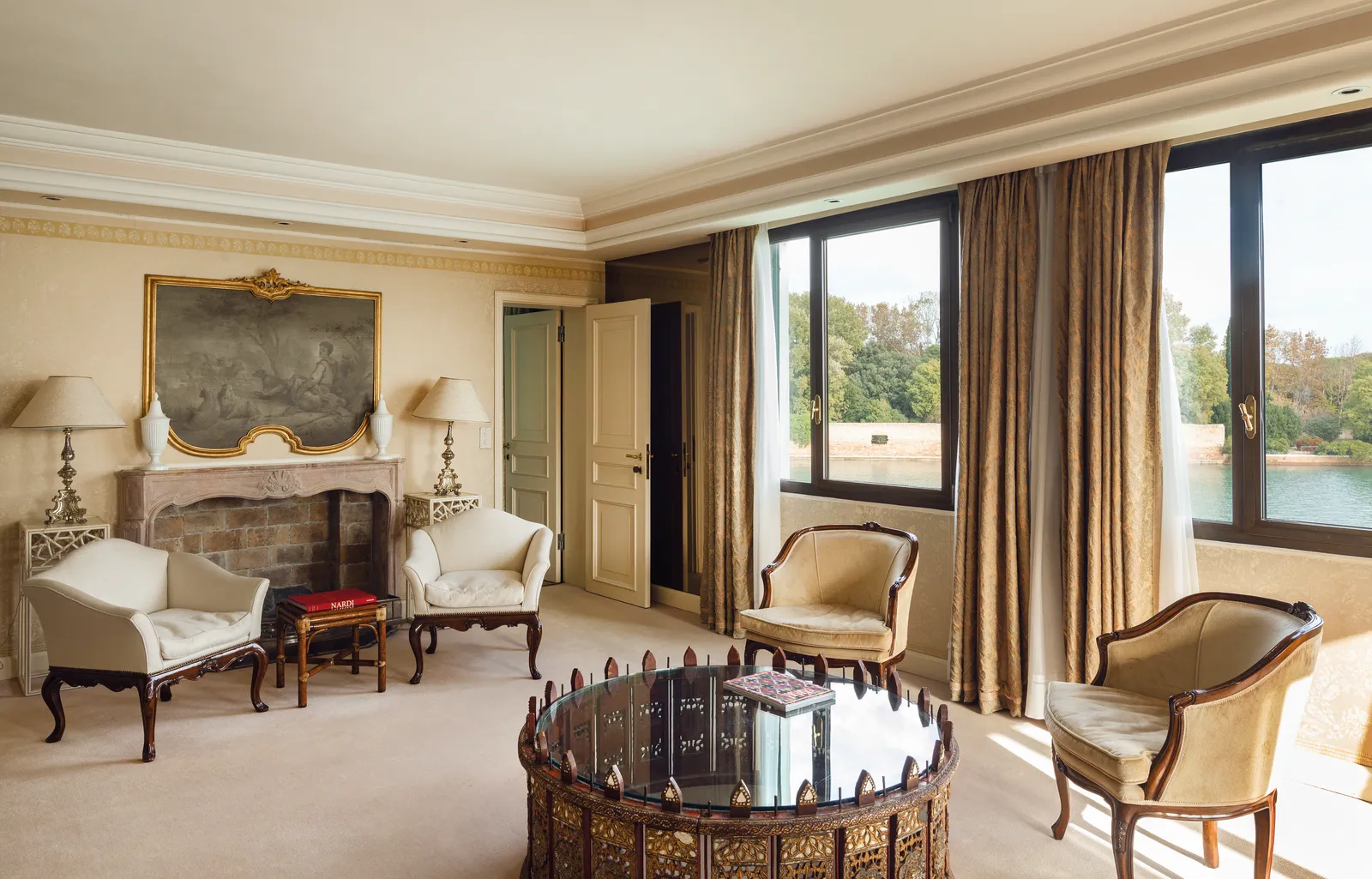 A San Giorgio Suite’s living room with a fireplace, armchairs around a round table and windows onto the water.