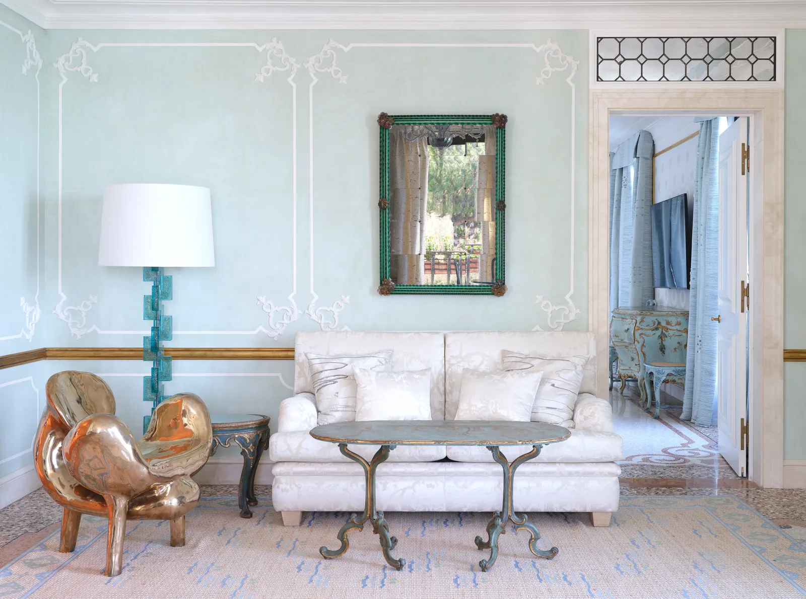 The Serenissima Suite’s living room: pale blue stuccoed walls, a white sofa, an iron table and a bronze sculpture chair.