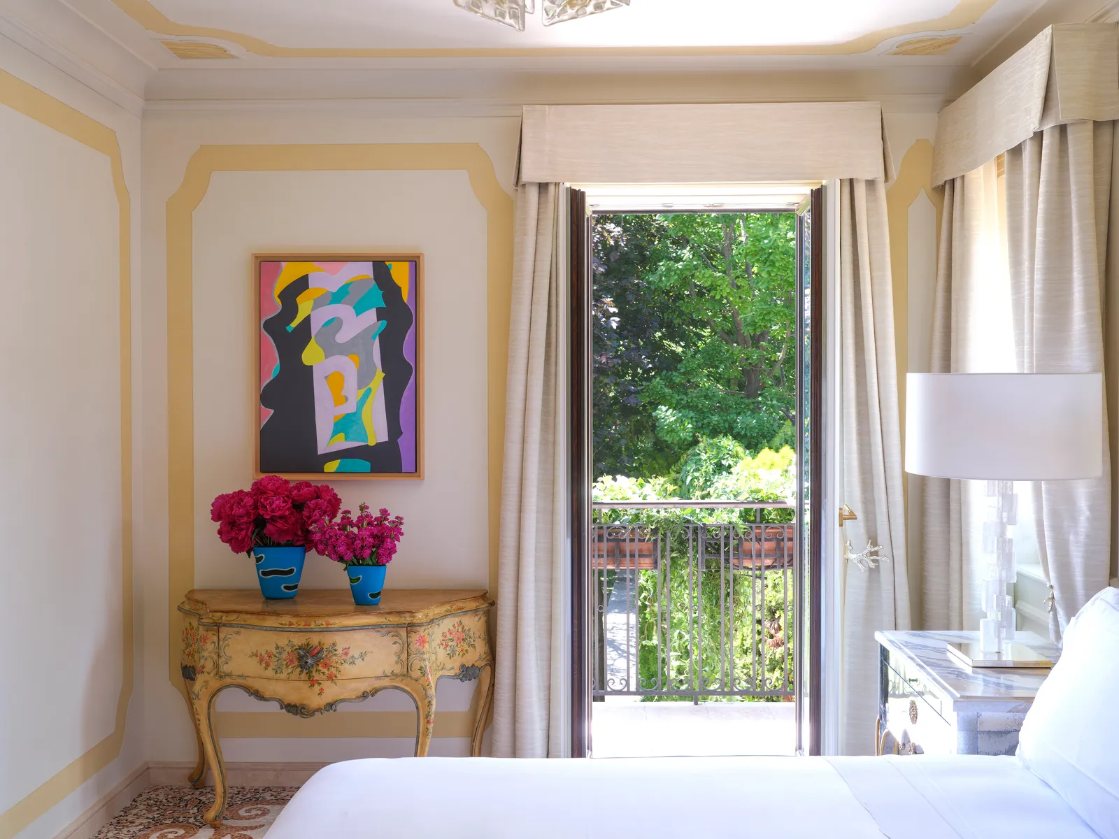 A Serenity Suite with an abstract painting over a painted console and the French window open onto the balcony and the trees.