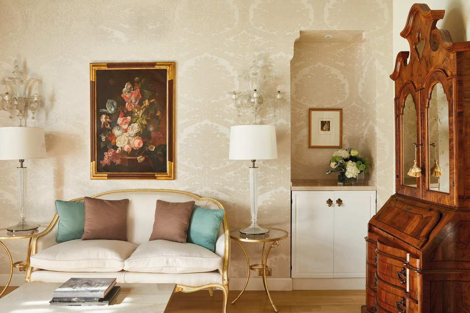 The sitting area of a junior suite in Palazzo Vendramin: a gilded settee with green cushions under a flower still life, and a walnut bureau.