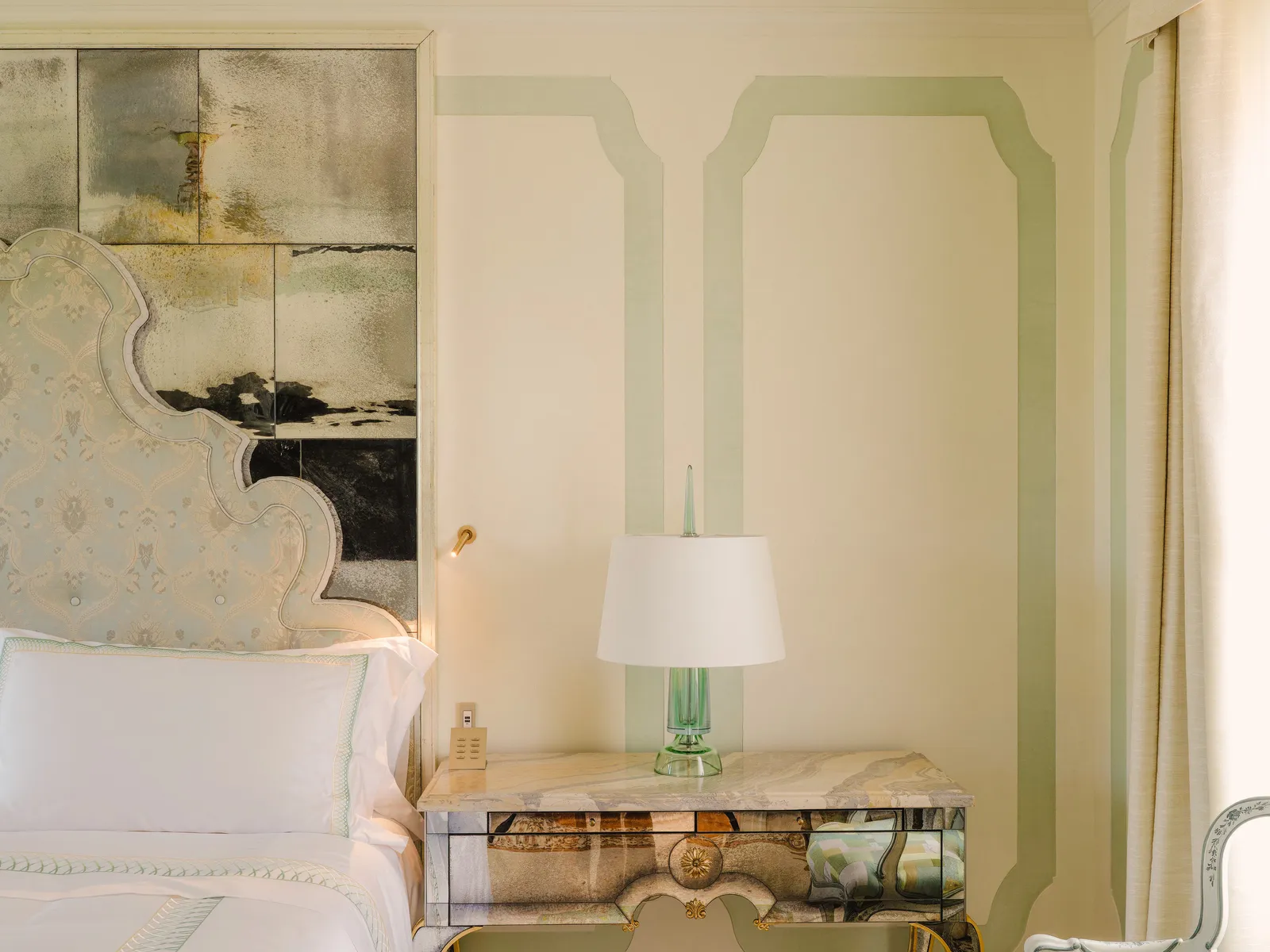 A Vigneto Suite’s bed, its pale fabric headboard against antiqued mirrors, with a marble bedside table.