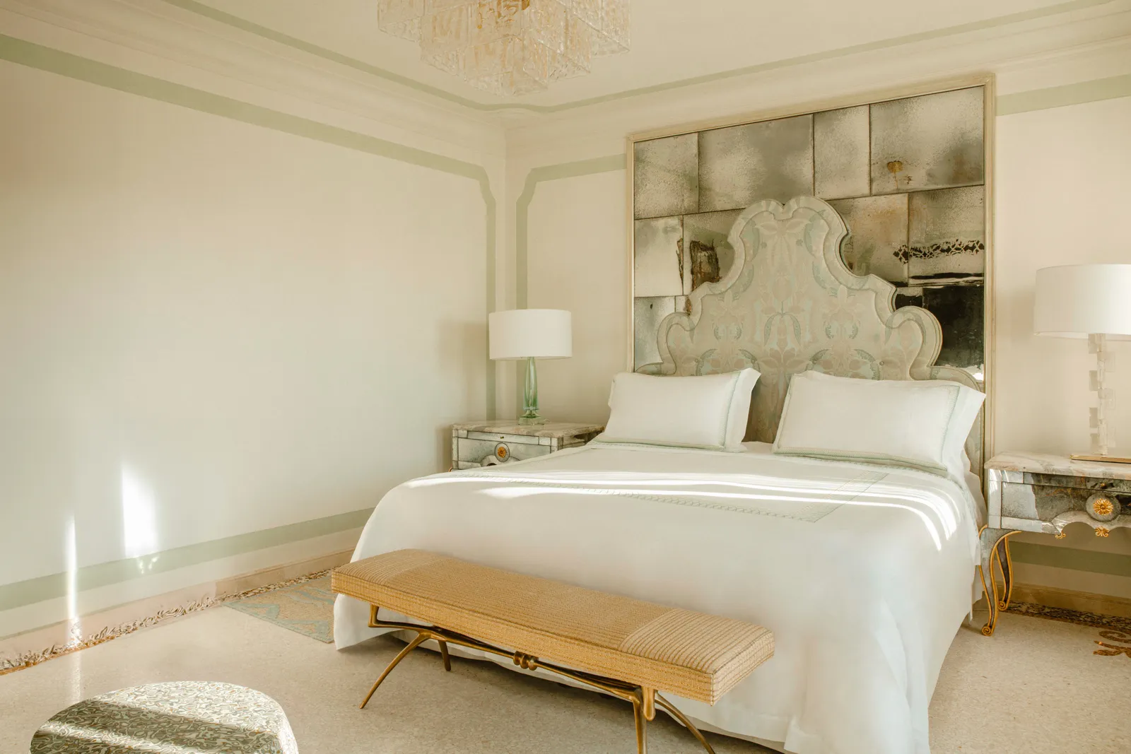 A Villeggiatura Junior Suite bedroom: the bed with its antiqued-mirror headboard and a gilded bench at its foot.