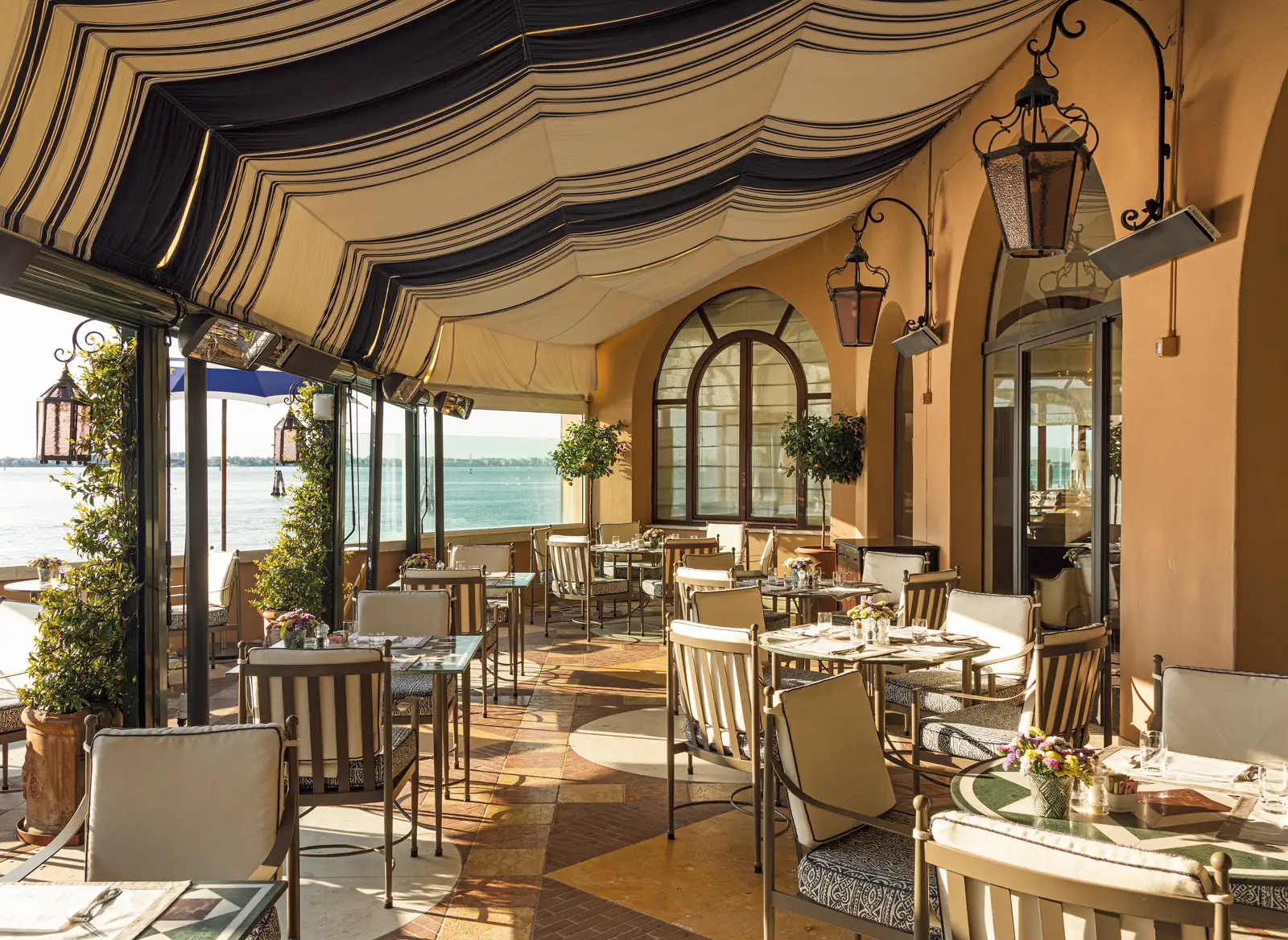 The San Giorgio’s covered terrace: tables under the striped awning, lanterns and the lagoon beyond the arches.