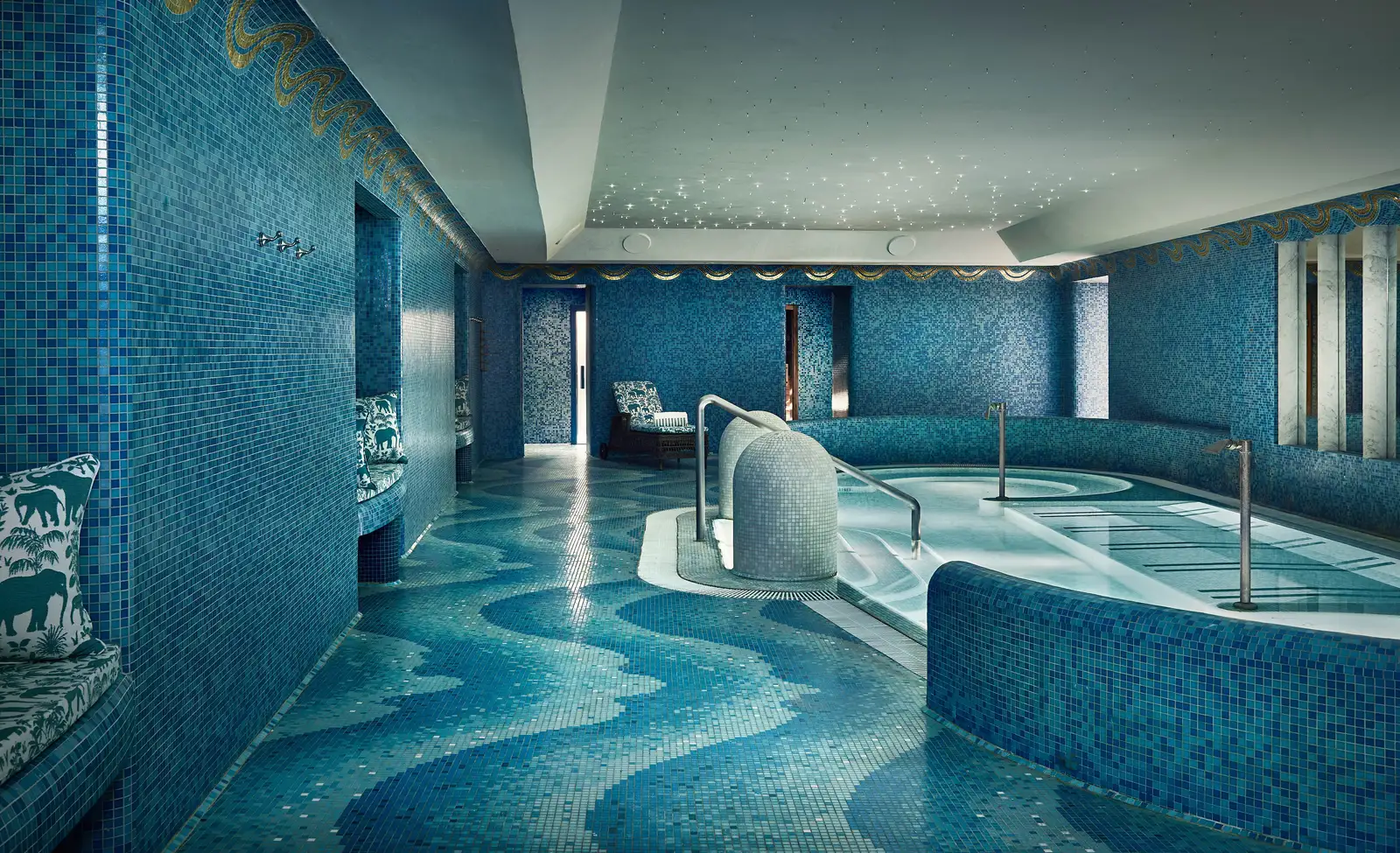 The spa’s pool: wave-patterned blue and turquoise mosaic on the floor and walls, the curved pool with steel handrails and a ceiling dotted with tiny lights; a cushioned bench in a niche on the left