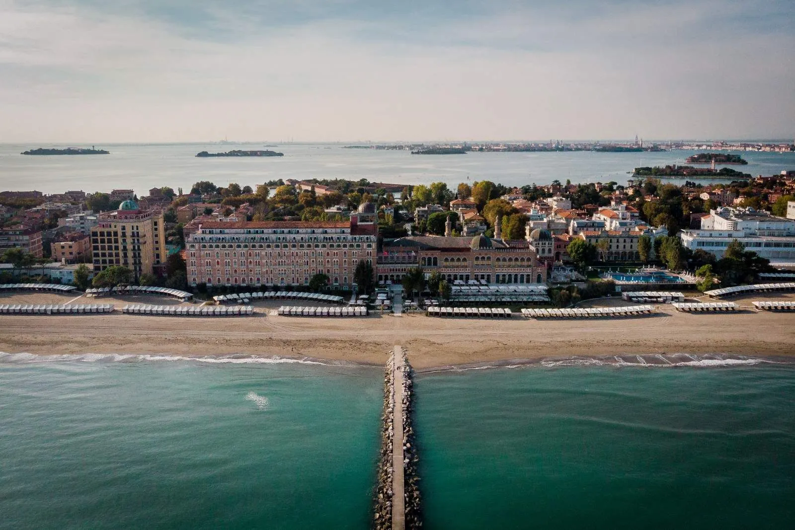 The Lido from above: the pier in the sea, the beach with its cabanas, the Excelsior, the island’s rooftops and the lagoon with its islands behind.