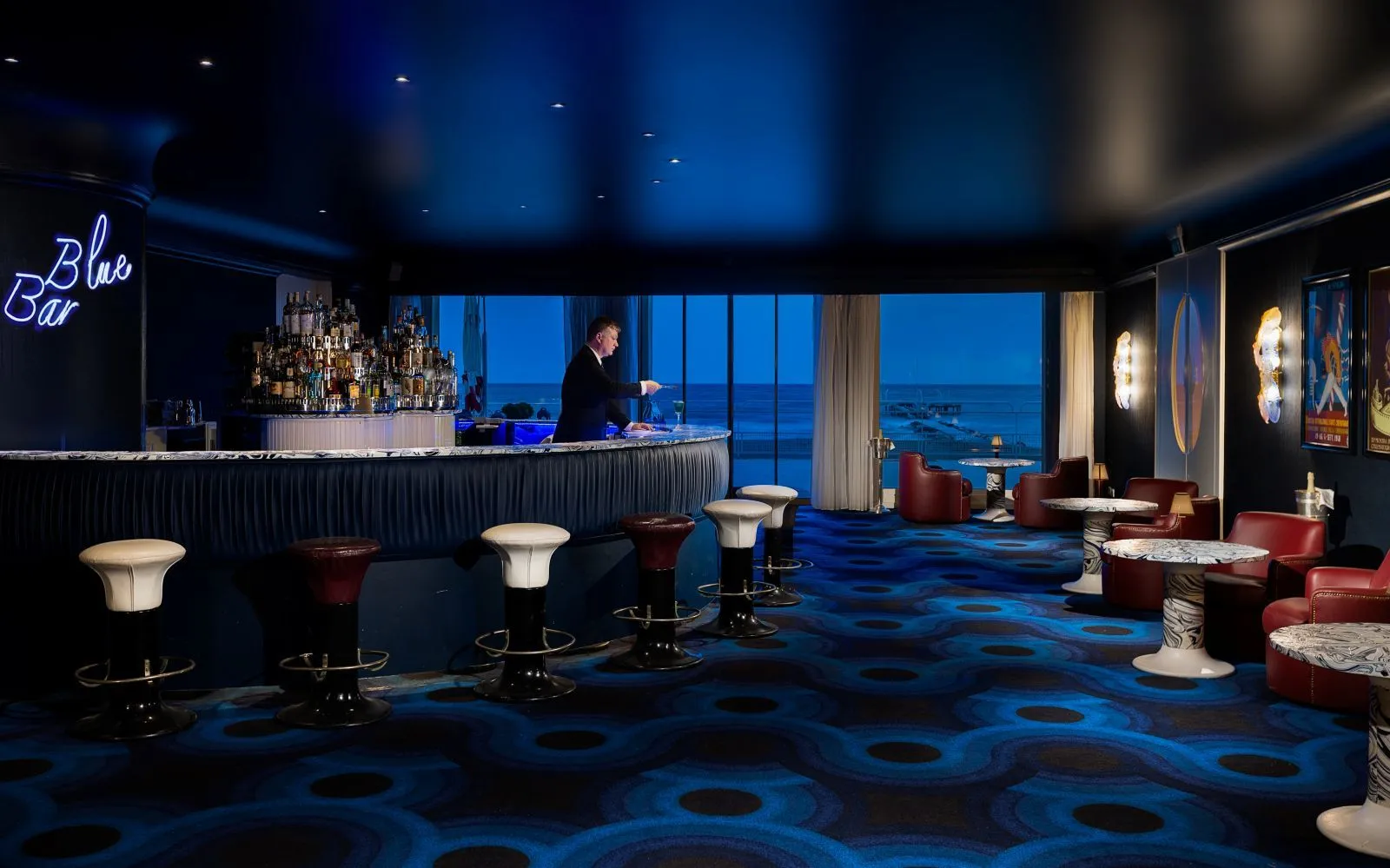 The Blue Bar: the curved counter, the stools, the neon sign, the blue carpet and the window onto the sea at dusk.