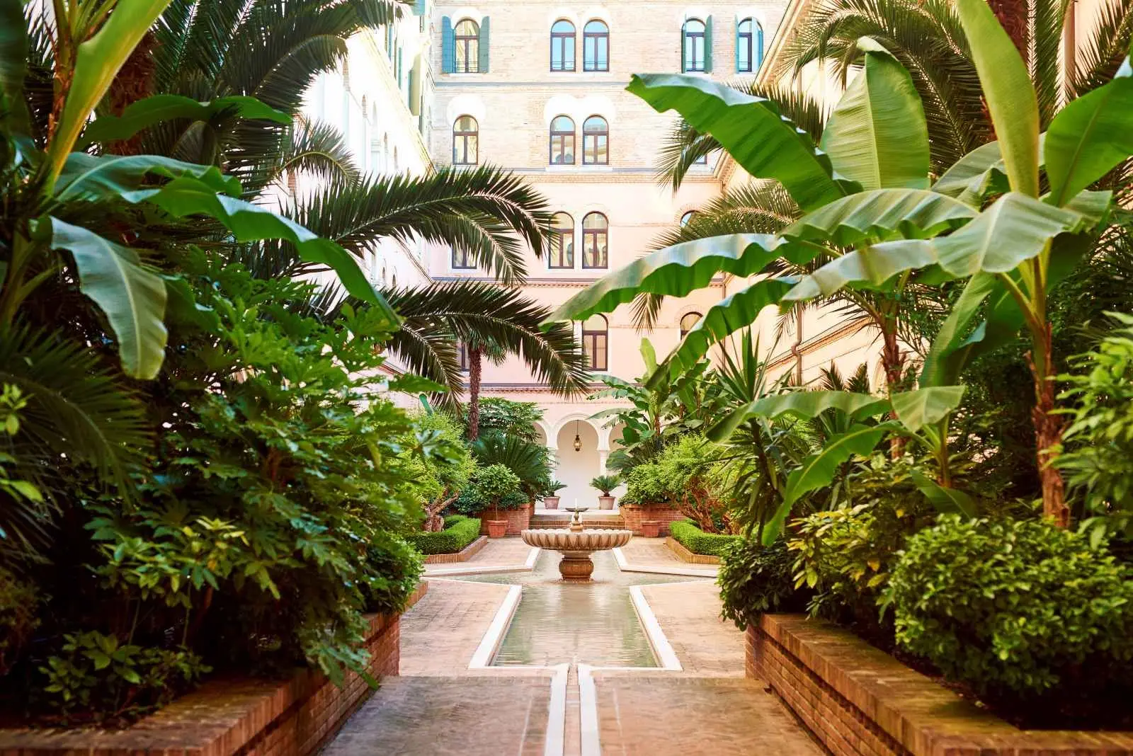 The inner courtyard garden: banana plants and palms either side of a water channel leading to a fountain, with the hotel’s windows above.
