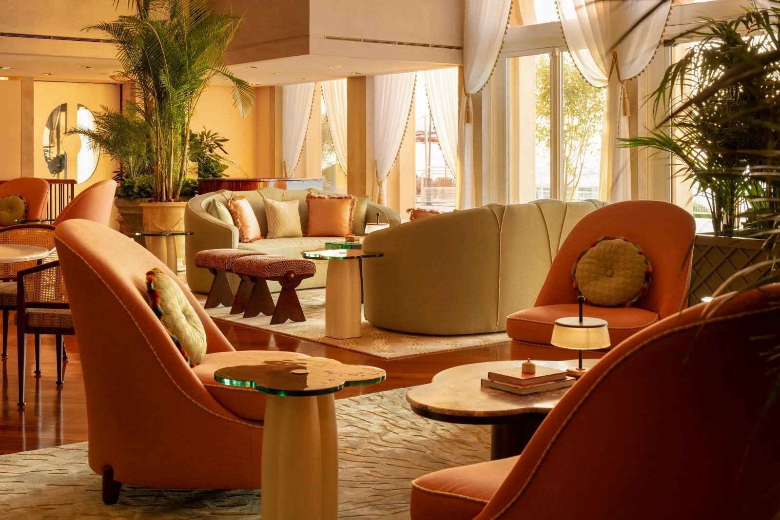 The Palm Court: orange armchairs, pale sofas, glass tables, potted palms and tall windows with white curtains.
