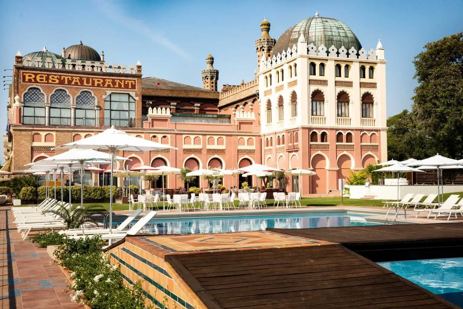 The outdoor pool with white loungers and umbrellas, in front of the pink-brick Moorish pavilion with its dome and Restaurant sign.