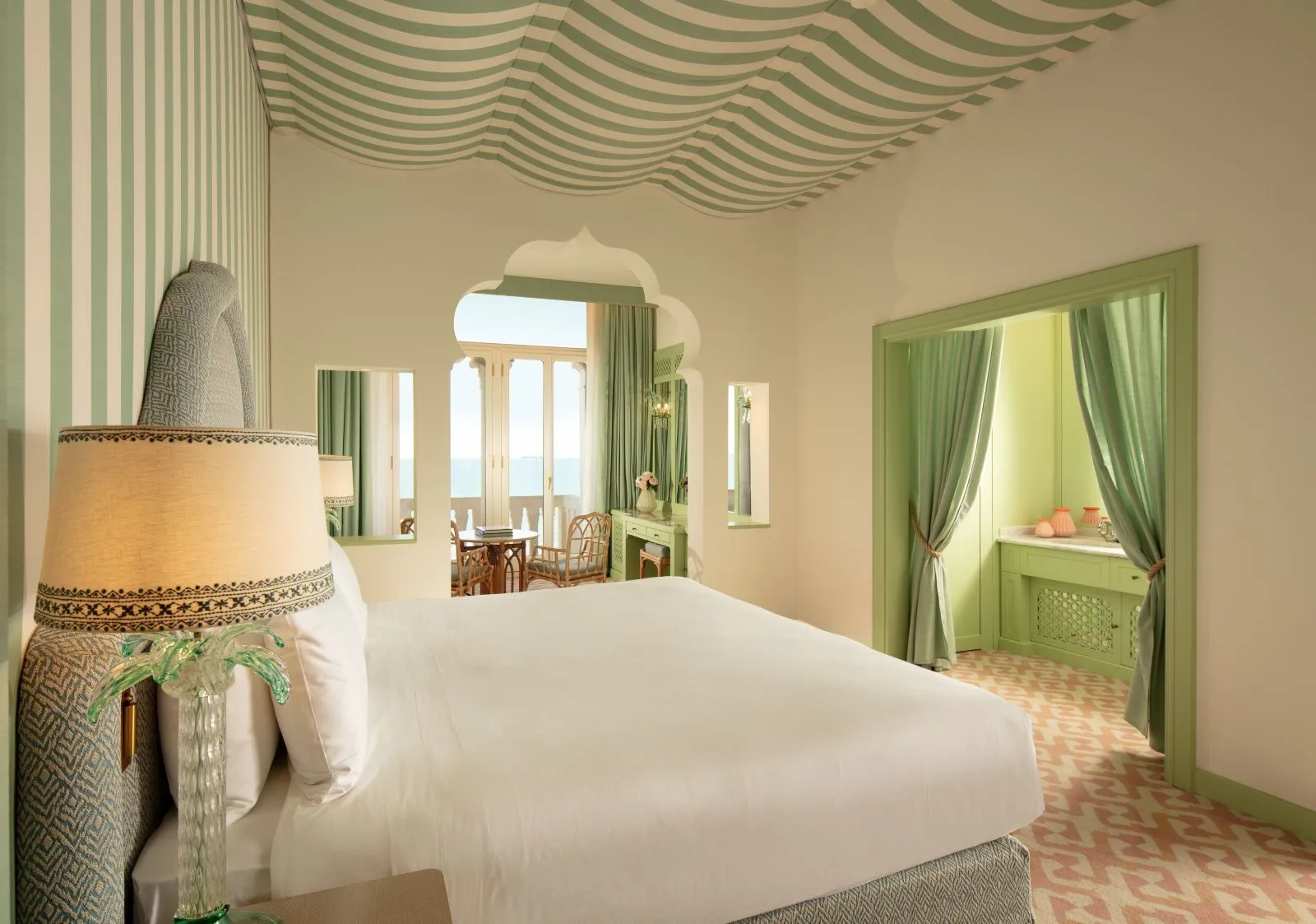 The bed in the foreground and, beyond a Moorish arch, the sitting nook with table and chairs by the window onto the sea.