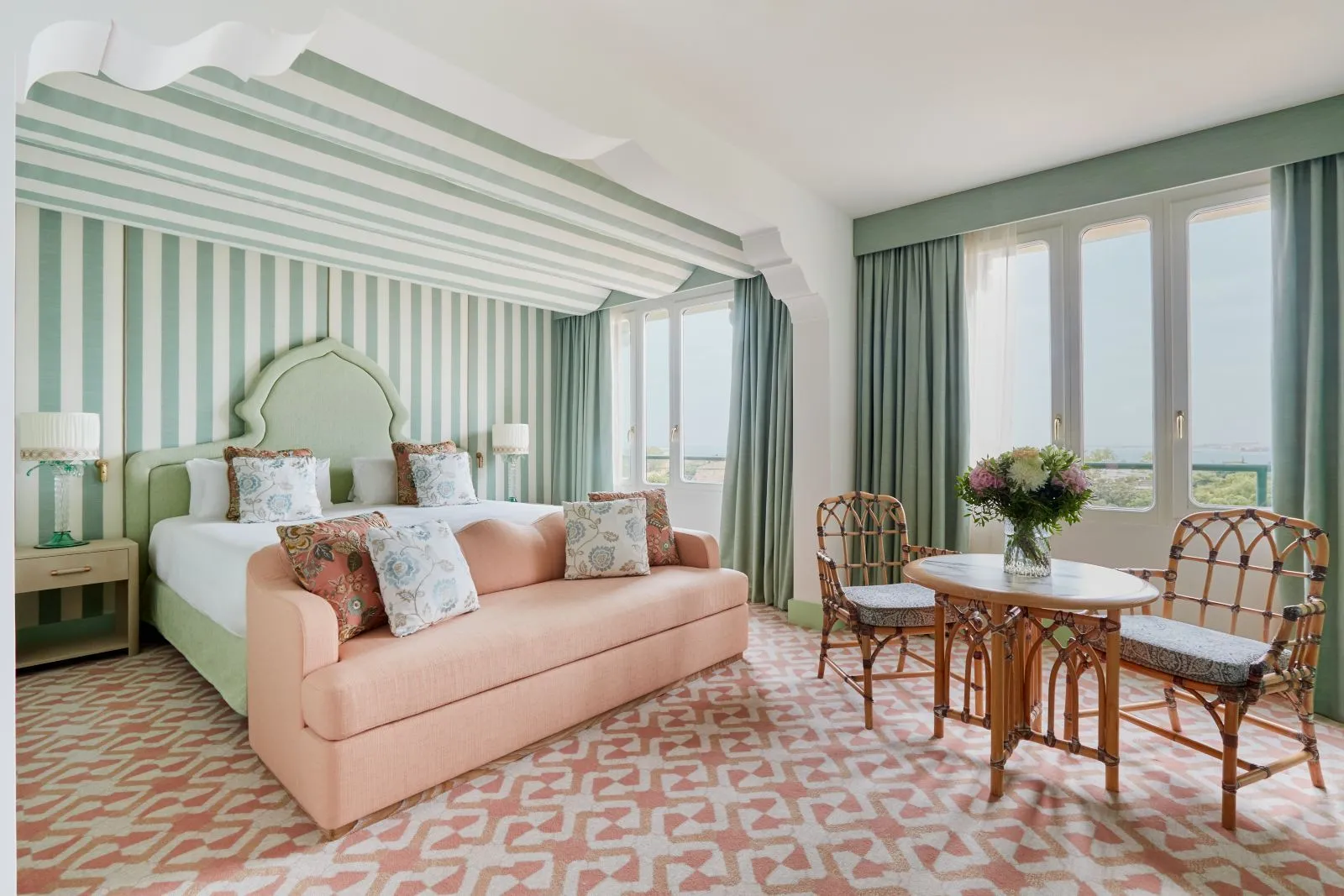 A green-striped room with a pink sofa at the foot of the bed, a table with flowers and windows over the lagoon.