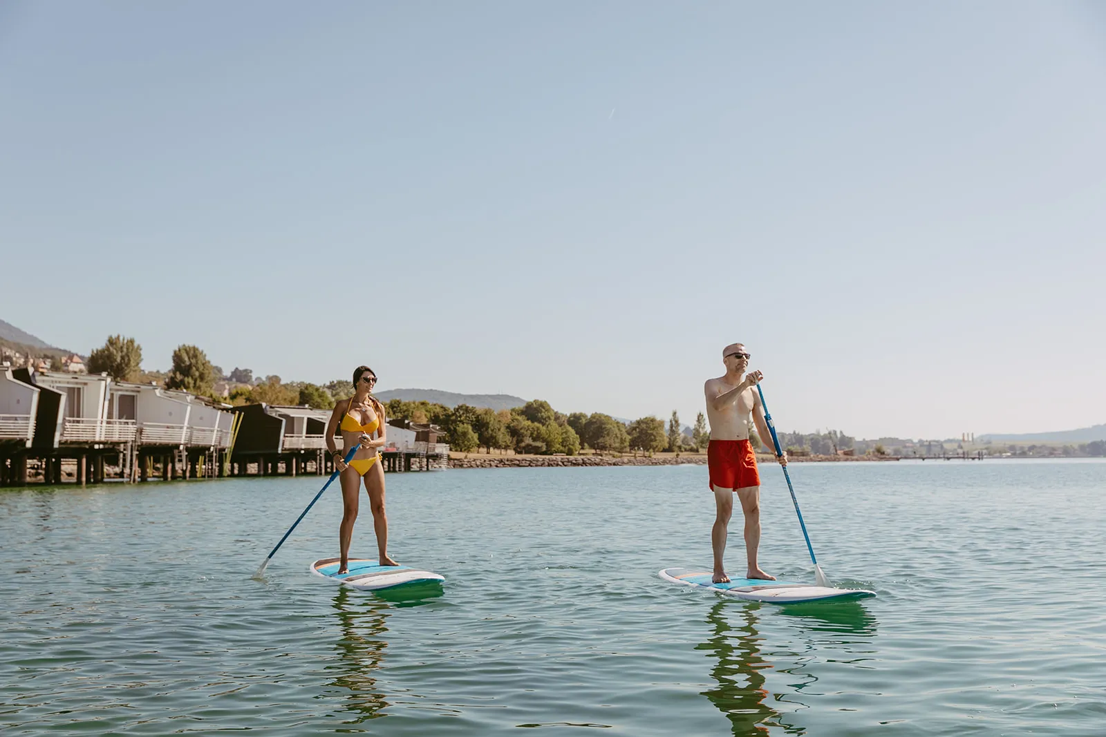 Two guests on stand-up paddleboards in front of the pavilions
