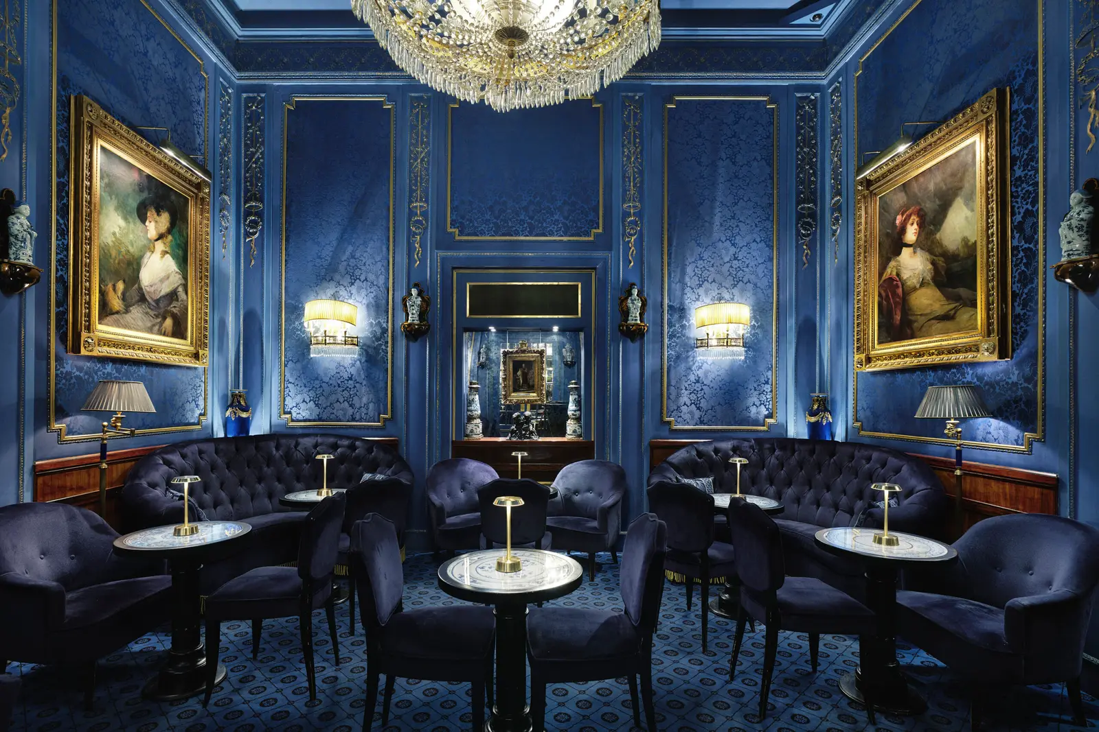 The Blaue Bar: blue velvet armchairs around small tables, blue brocade walls with 2 gilt-framed portraits and a crystal chandelier.