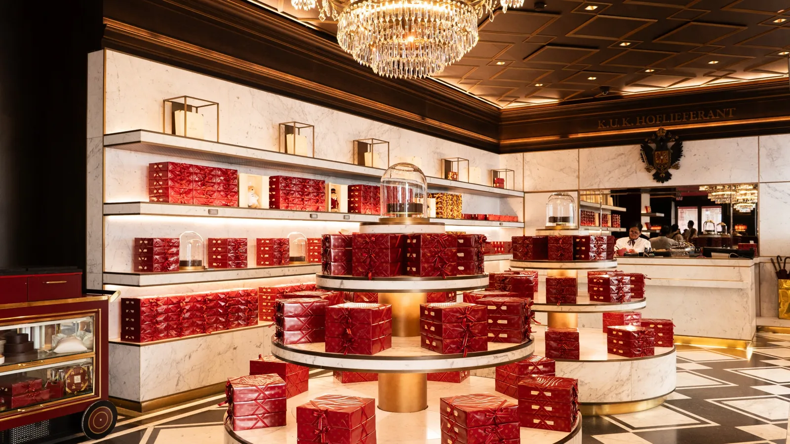 The Sacher Confiserie: marble counters and shelves stacked with red boxes of Original Sacher-Torte under a crystal chandelier.