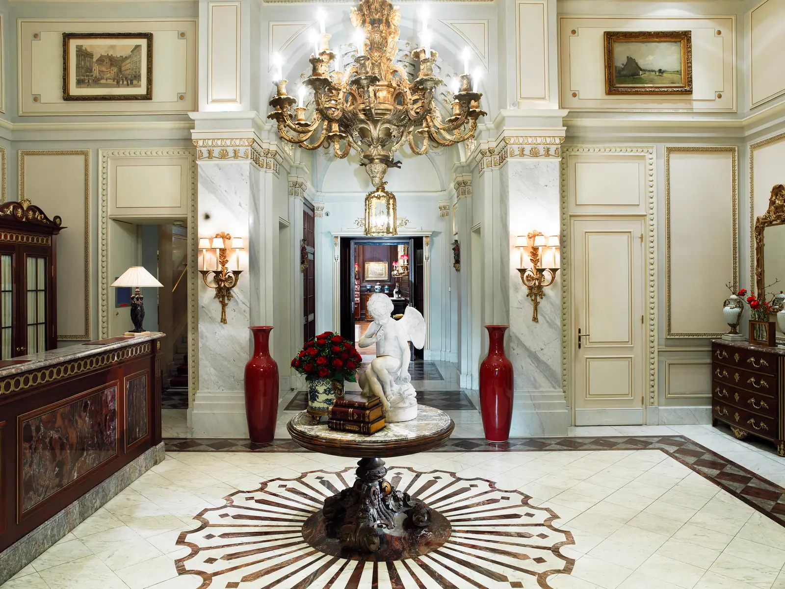The entrance hall: a gilt chandelier, a marble floor with a sunburst inlay and a white sculpture on a table at its centre.
