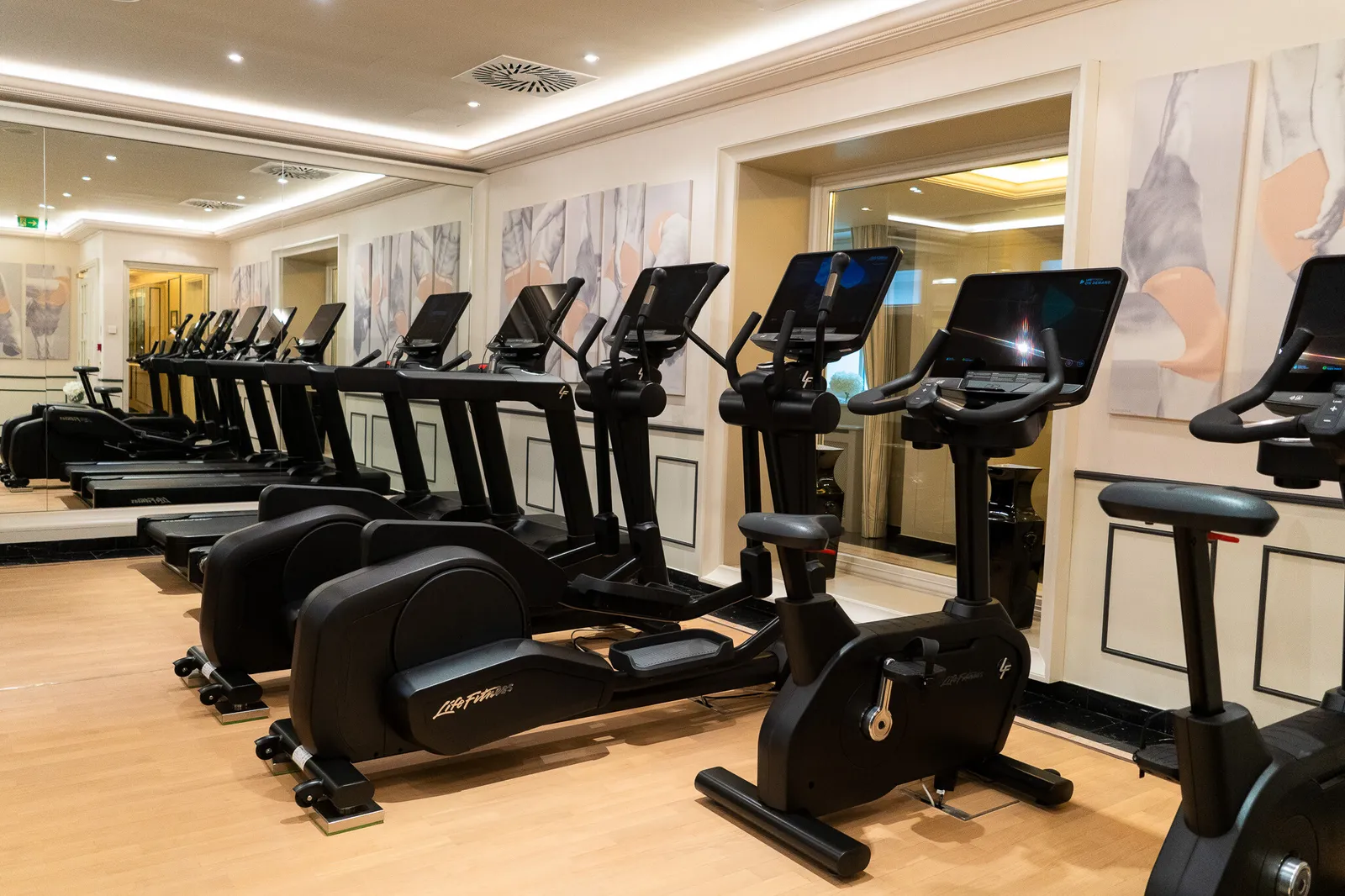 The fitness room: a row of treadmills, cross-trainers and exercise bikes on a pale wooden floor.