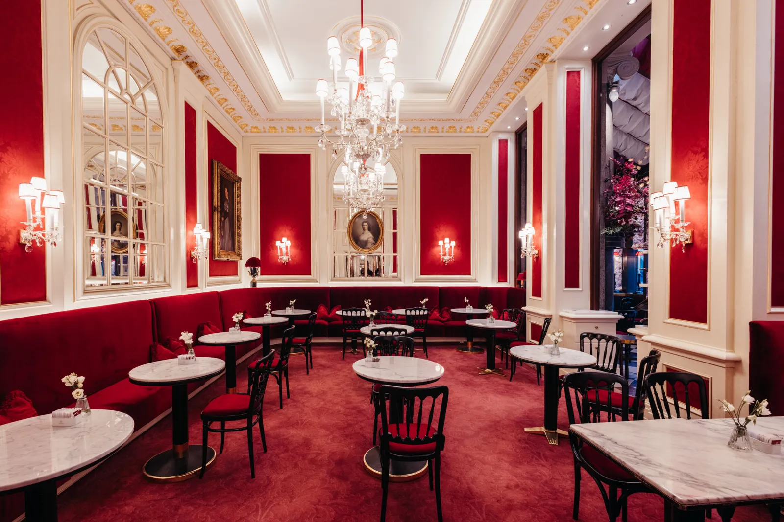 The Café Sacher room: red velvet banquettes, marble-topped tables, arched mirrors and a crystal chandelier.