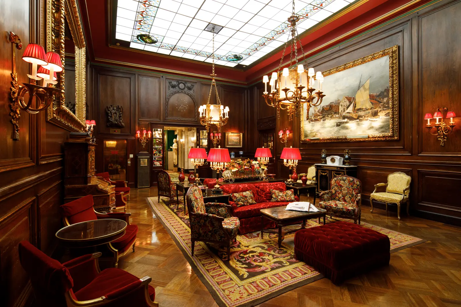 The lobby: dark panelling, red armchairs and sofas, a large painting in a gilt frame and the glass skylight.